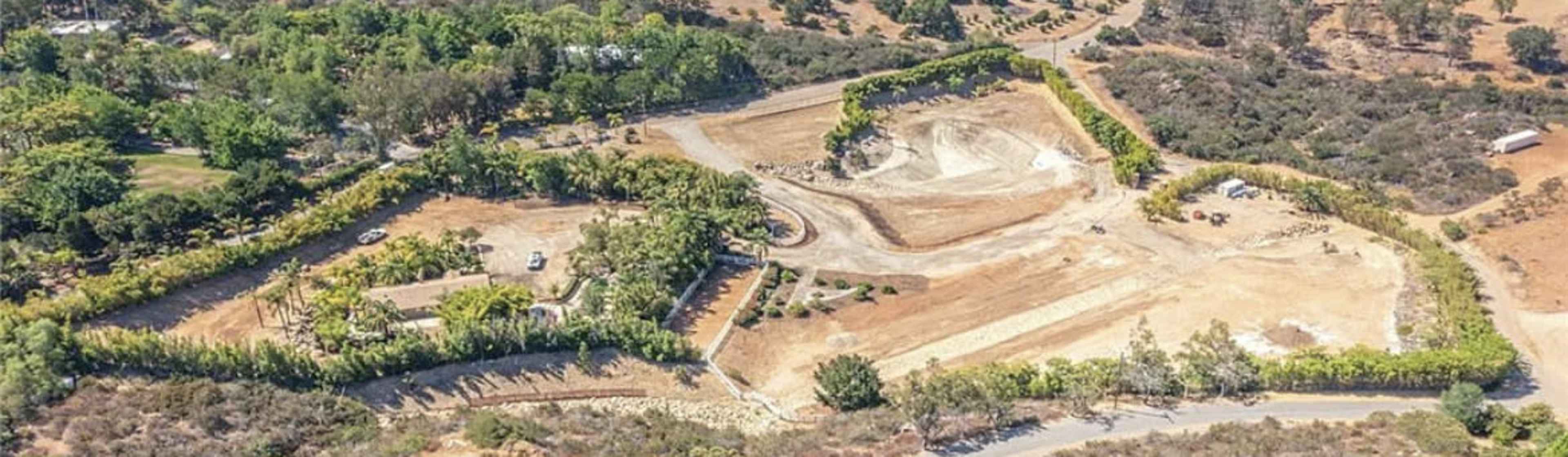 The aerial view shows a partially developed area with cleared land, vegetation, and a winding road.