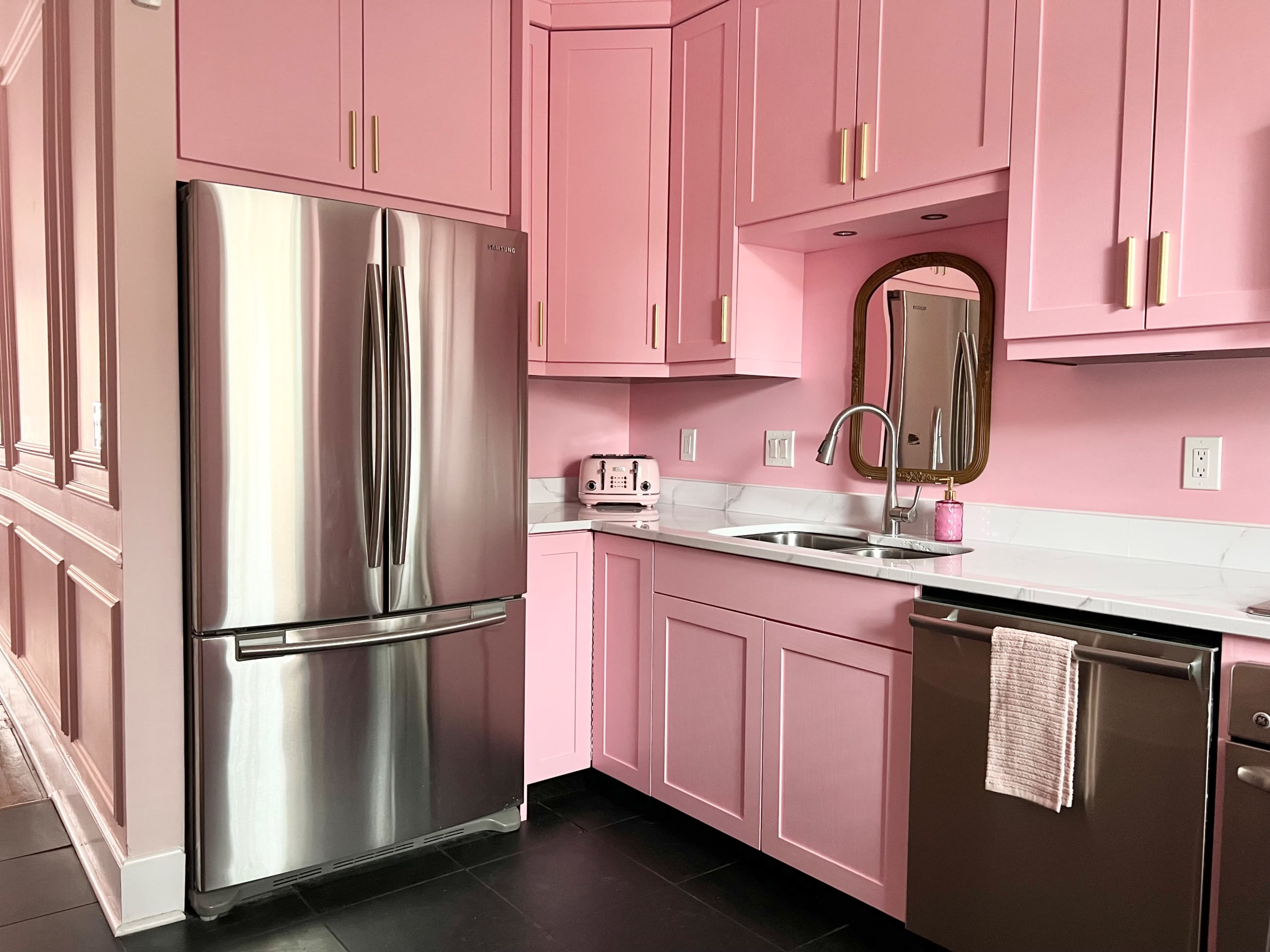 A kitchen with pink cabinetry, a stainless steel refrigerator, and a countertop sink.