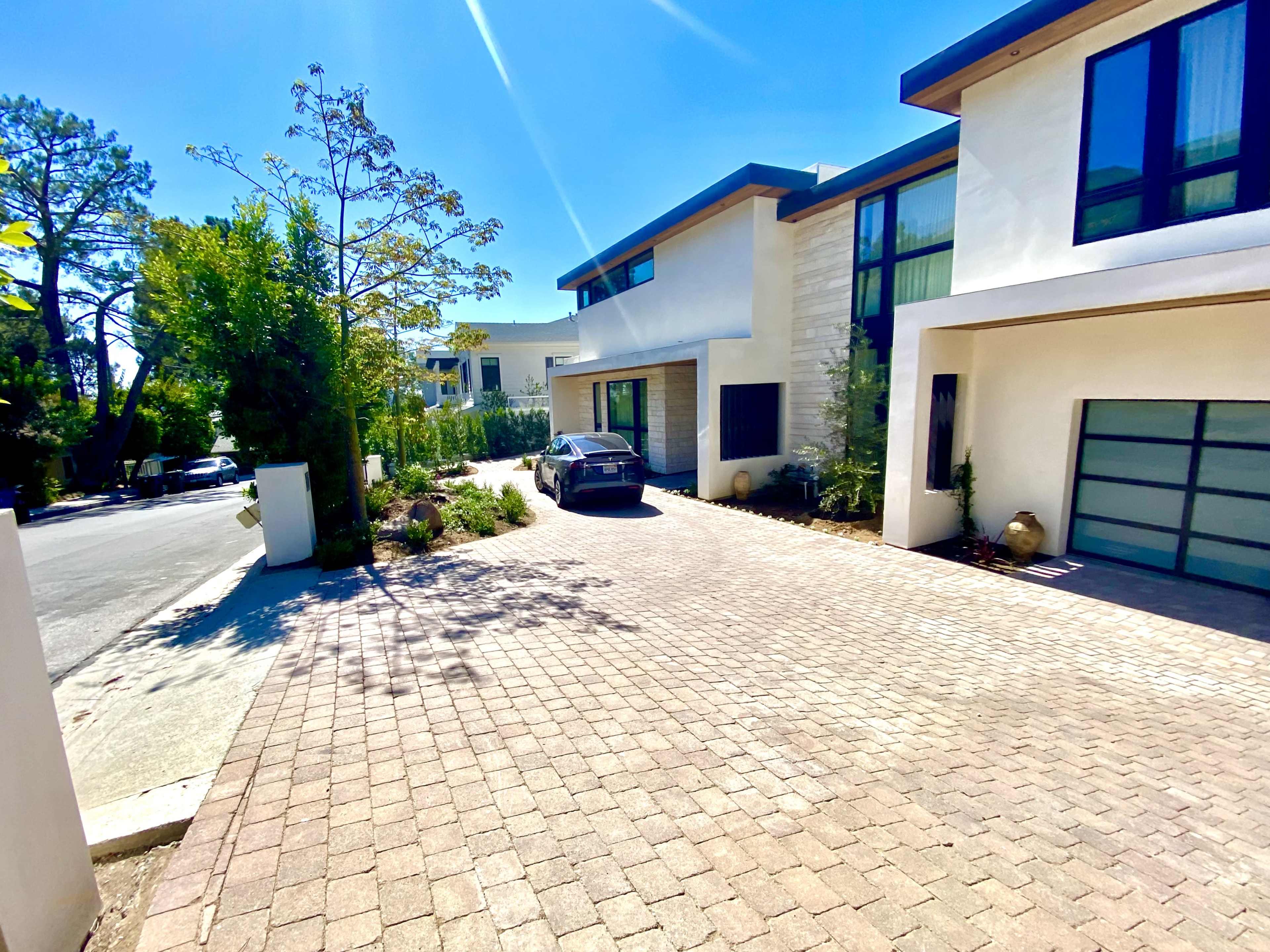 A modern house with a paved driveway and a car parked in front, surrounded by landscaping.