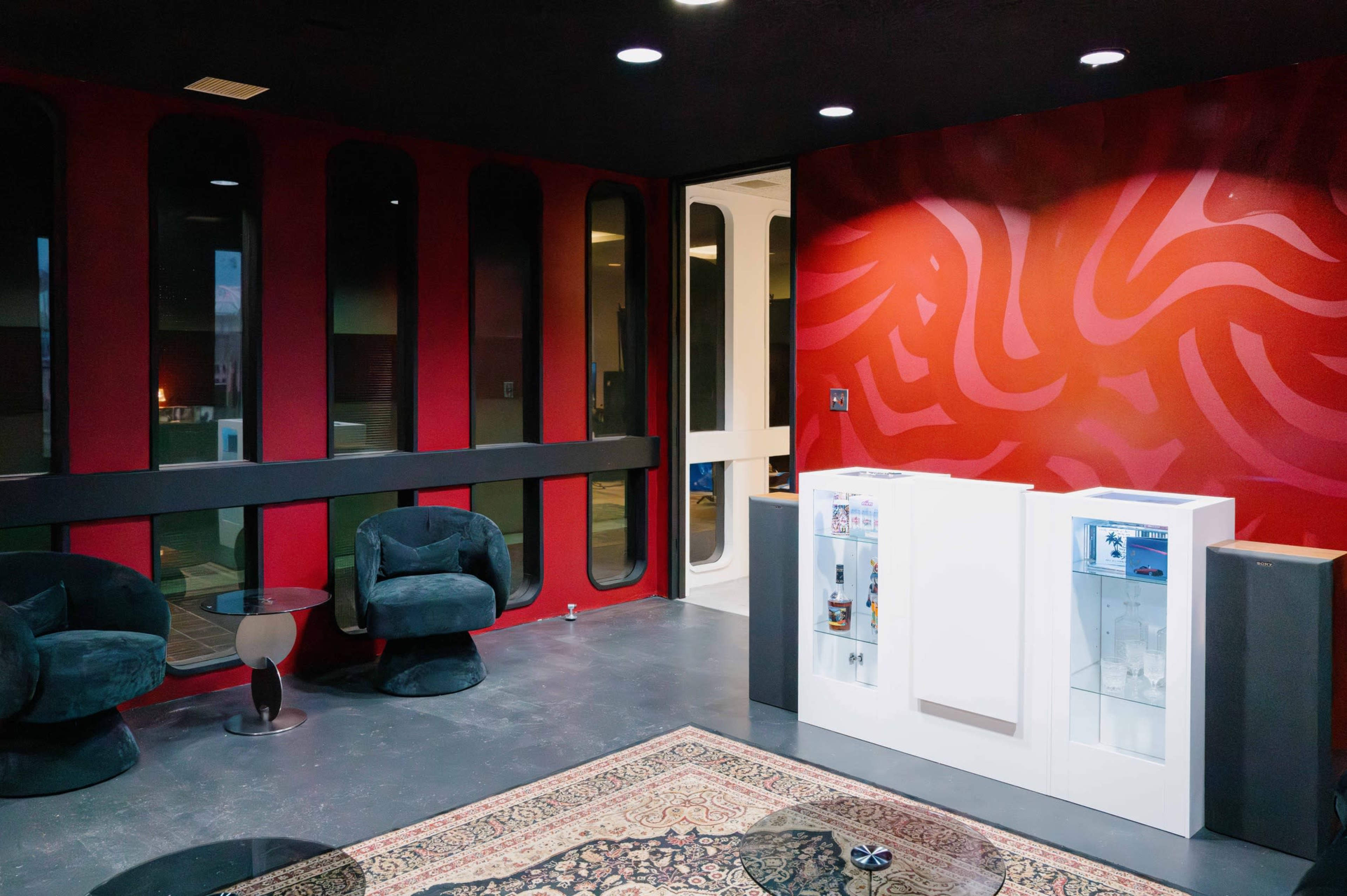 The image depicts a modern interior with two black chairs, a white water cooler, and a red patterned wall.