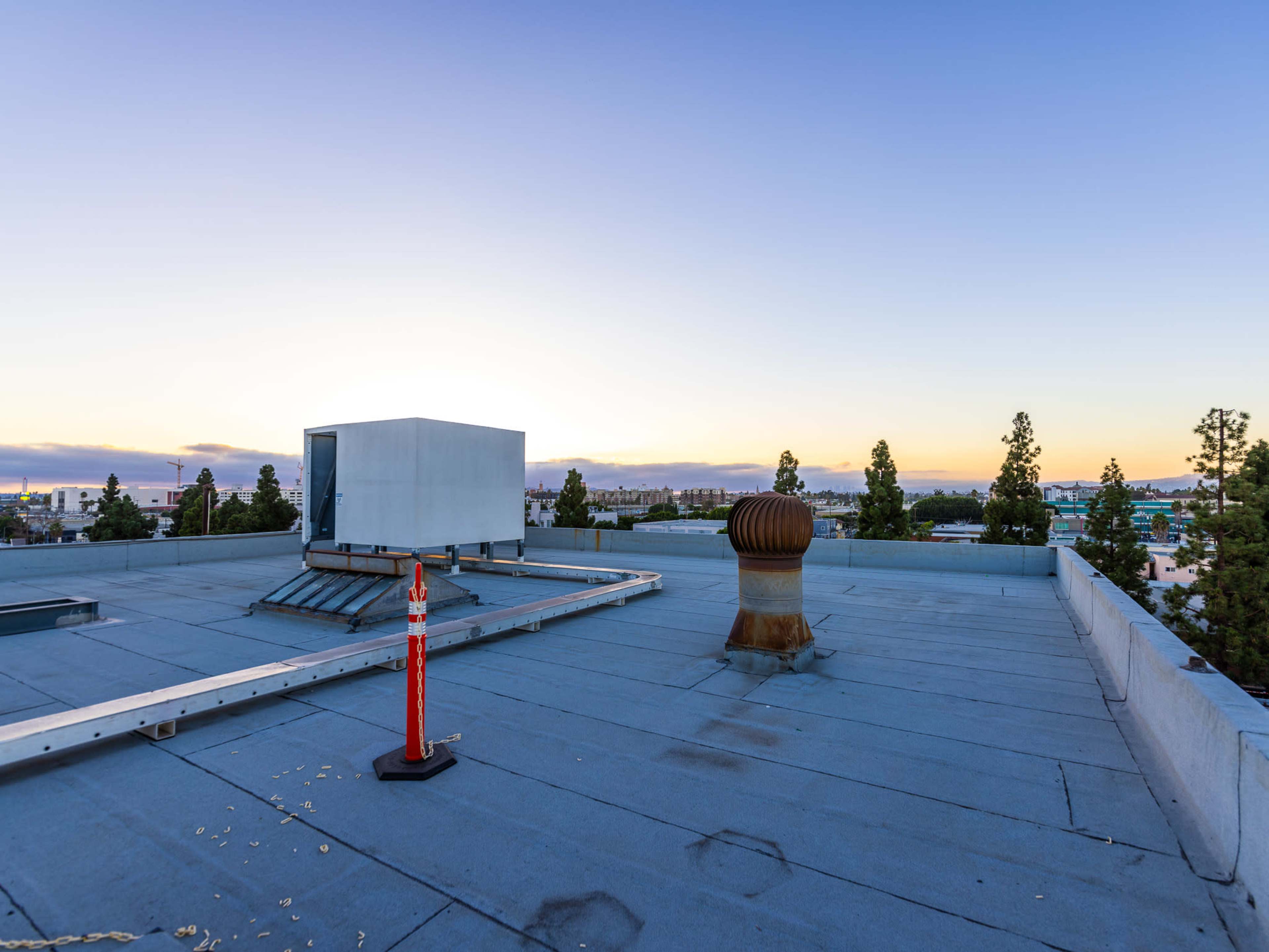 A flat rooftop with mechanical equipment, a ventilation system, and a clear sky at sunset in the background.