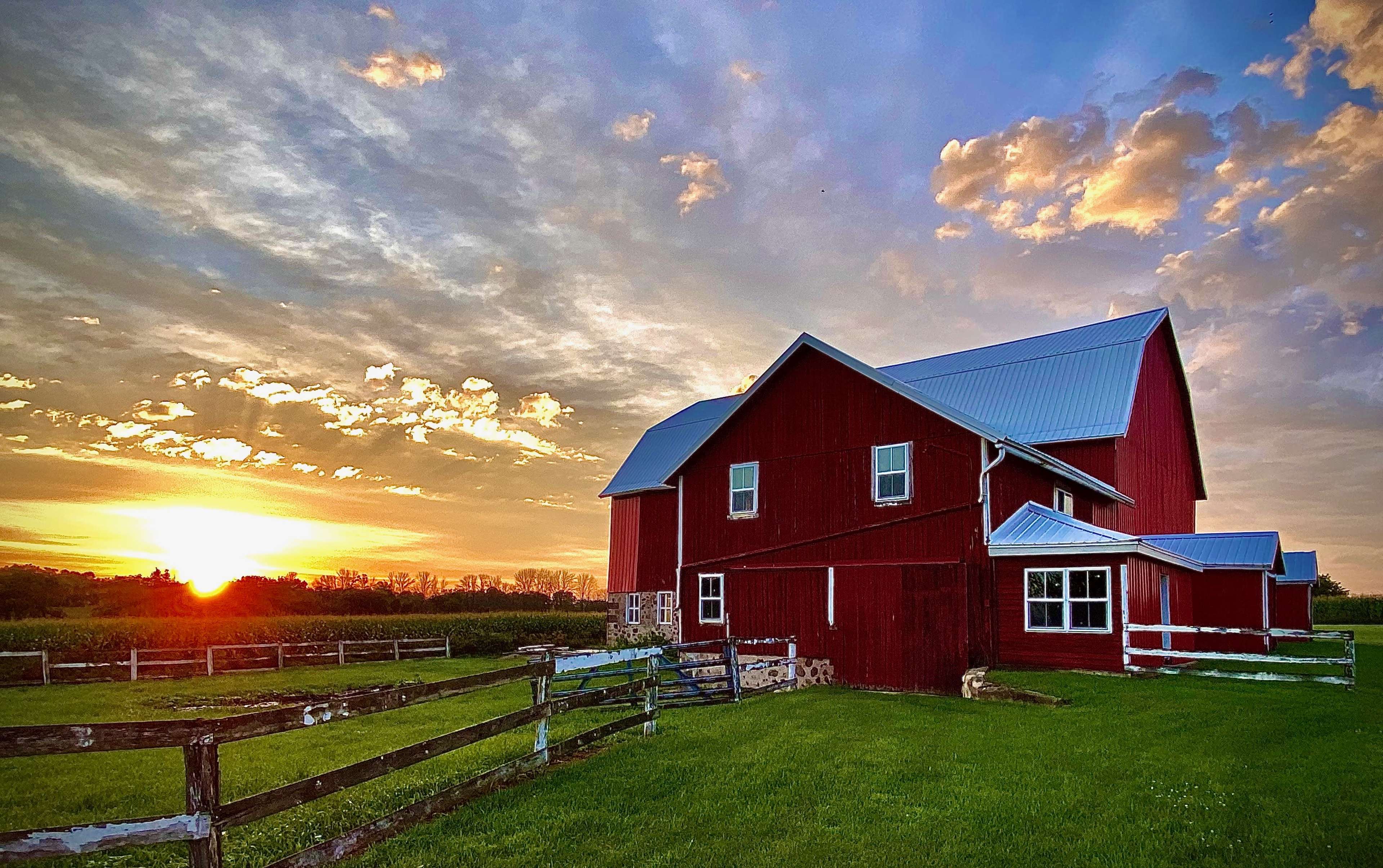 A red barn stands in a green field under a cloudy sunset sky.