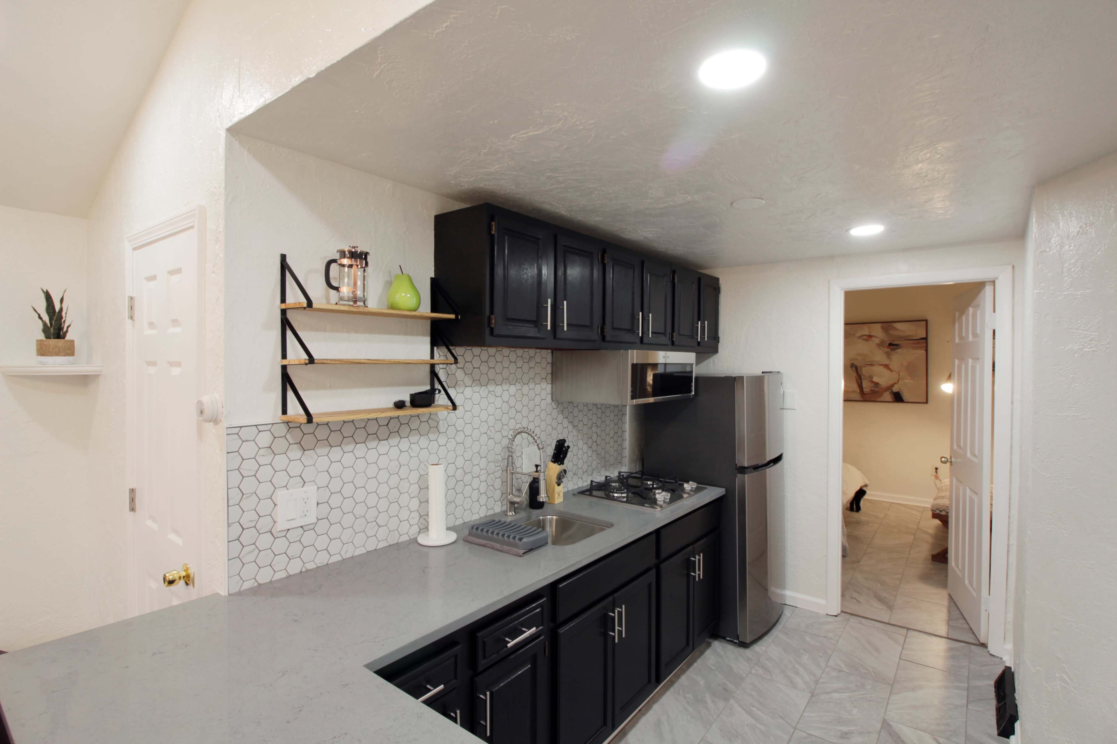 A modern kitchen featuring dark cabinetry, a gray countertop, and a hexagonal tile backsplash, with a doorway leading to another room in the background.