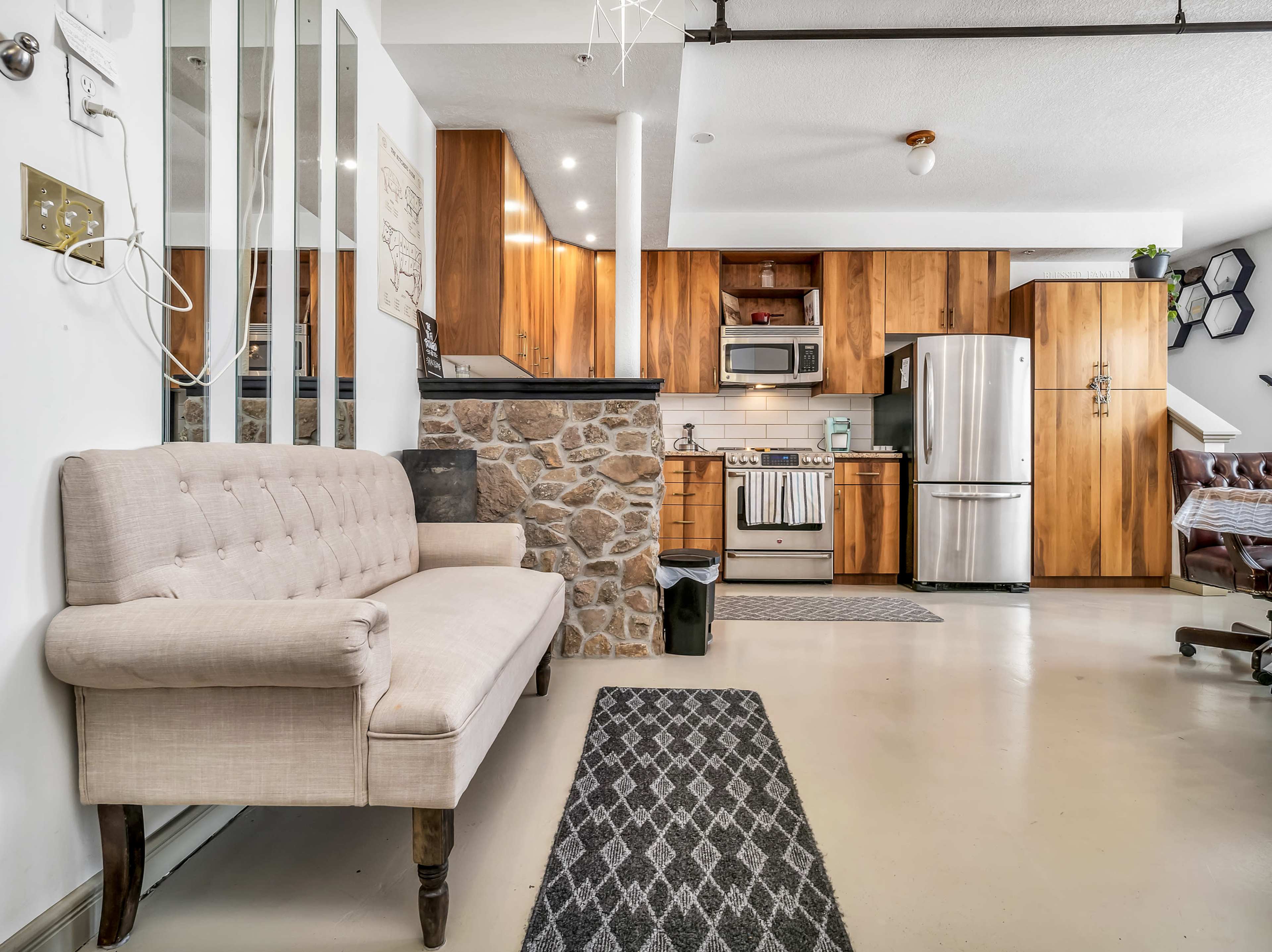 A modern kitchen and living area featuring wooden cabinetry, a beige sofa, and a stone accent wall.