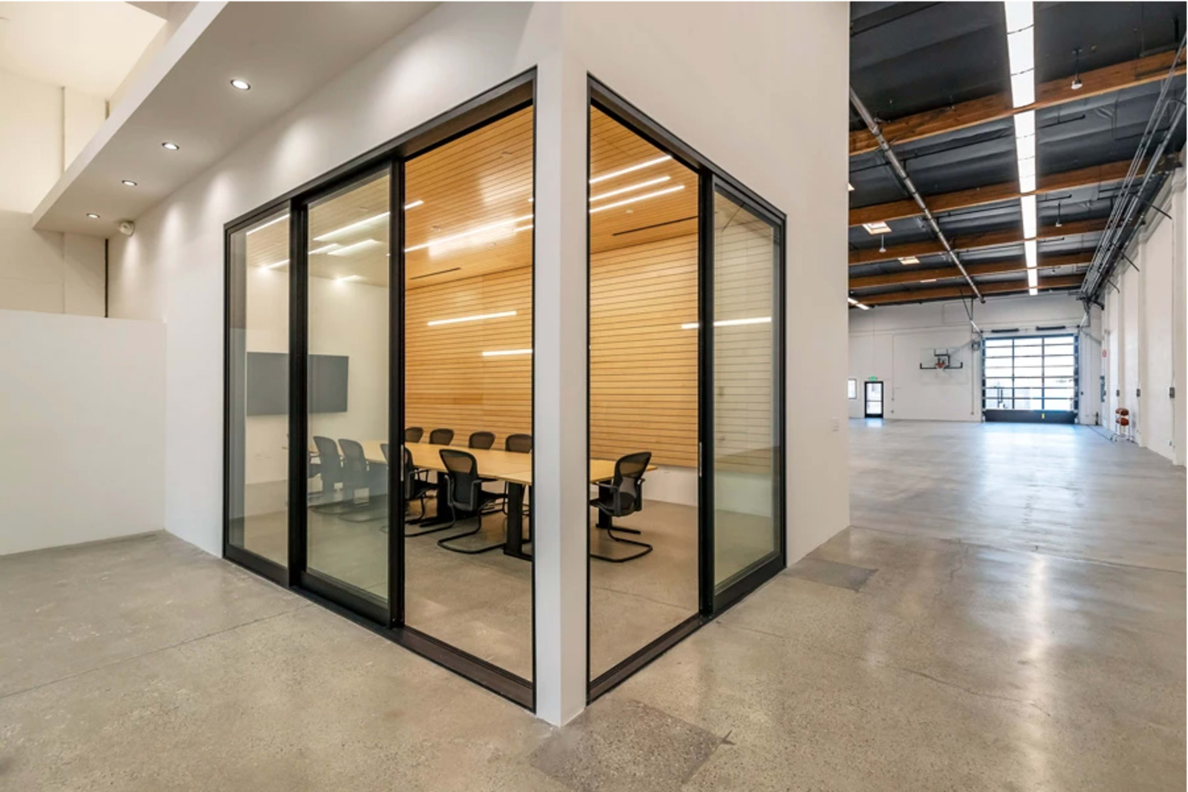 A modern conference room with glass walls and a wooden accent wall, located in a spacious industrial-style interior.
