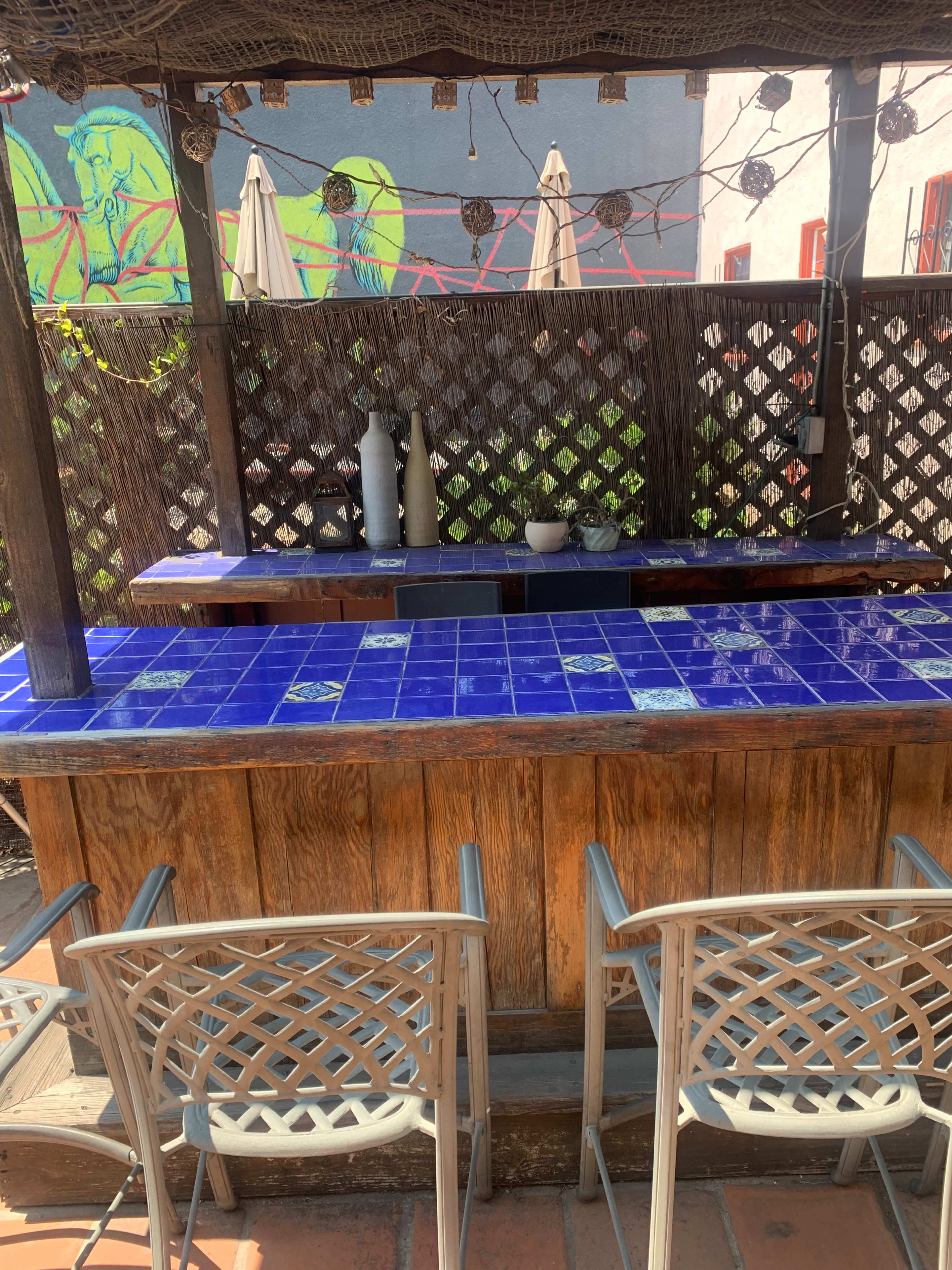 An outdoor bar area with a blue tiled countertop, wooden structure, and two metal chairs.