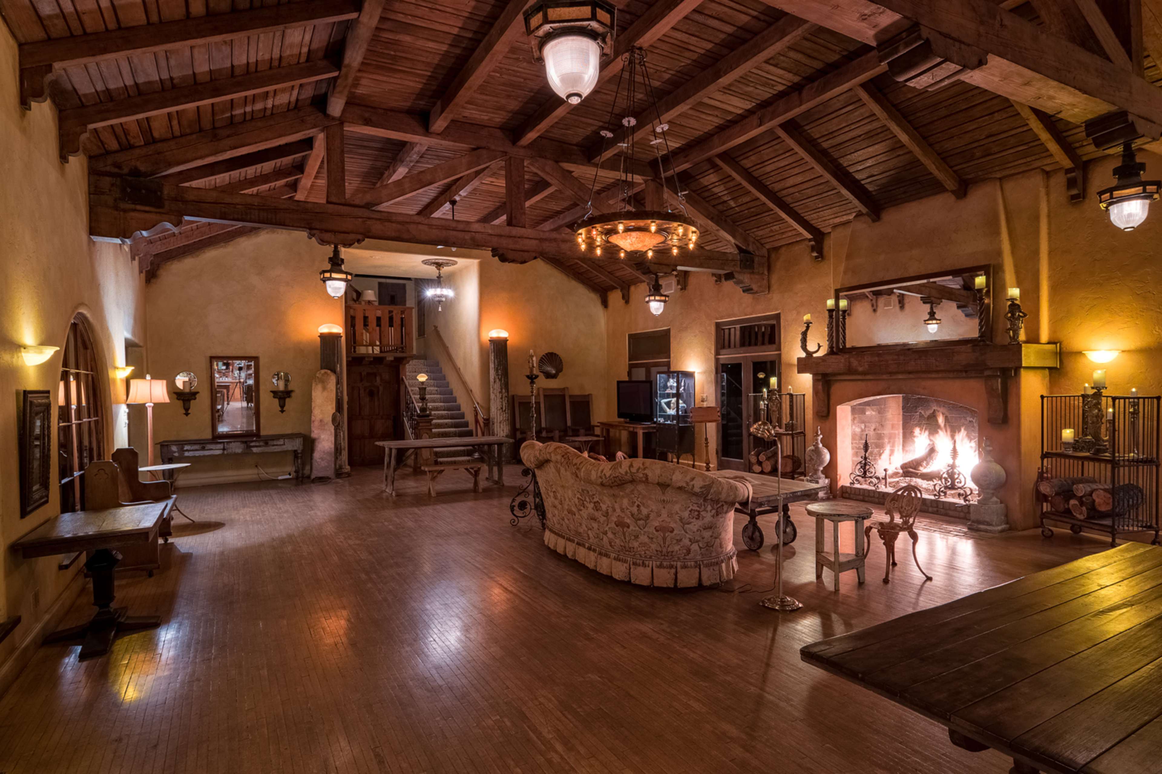 A spacious living area with wooden beams, a central fireplace, and various antique furnishings.
