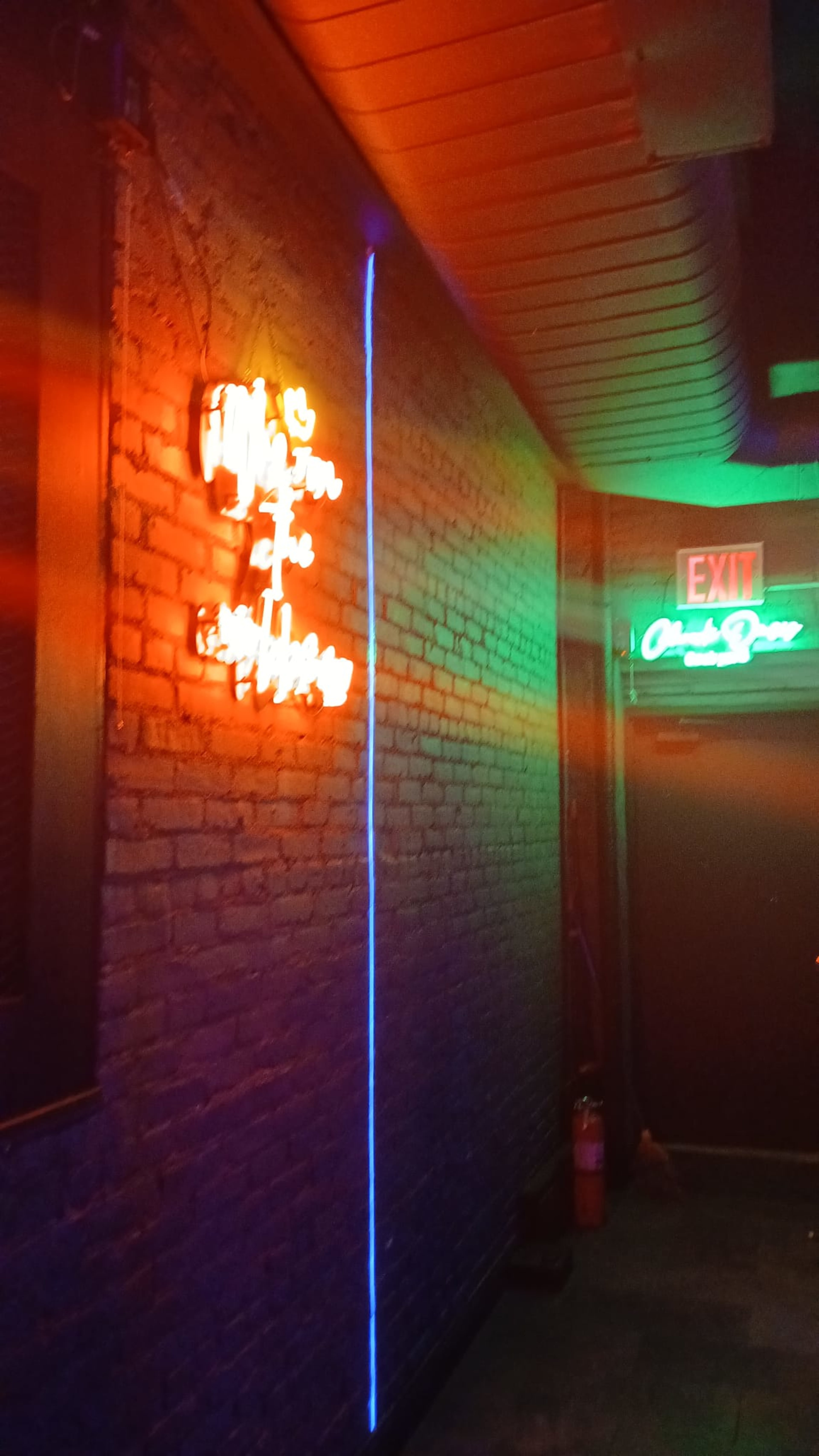 The image shows a dimly lit hallway with neon signs on a brick wall, including one that reads "Hello from the other side" and another that indicates an exit.