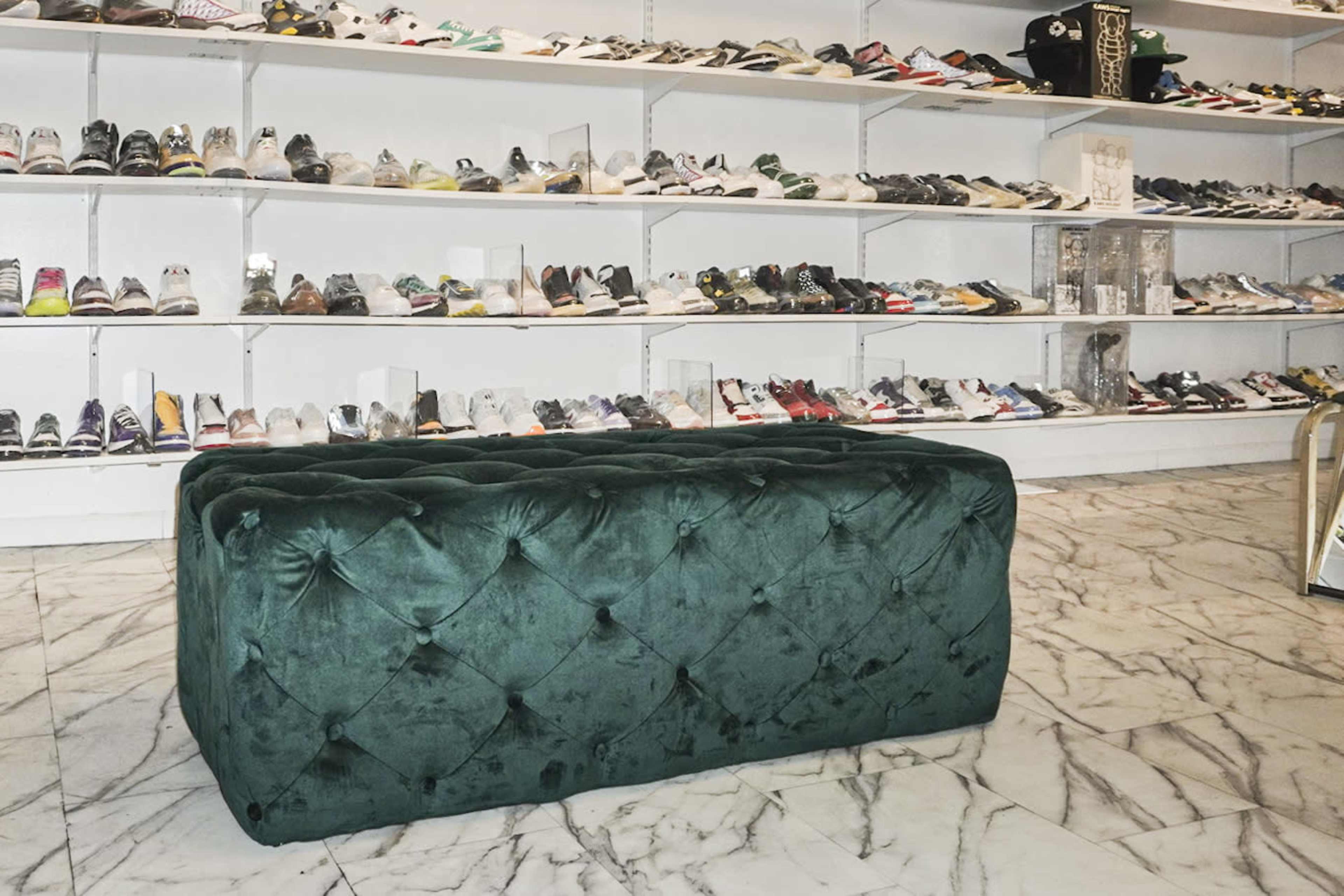 A plush green ottoman in front of a wall of neatly arranged shoes on shelves.