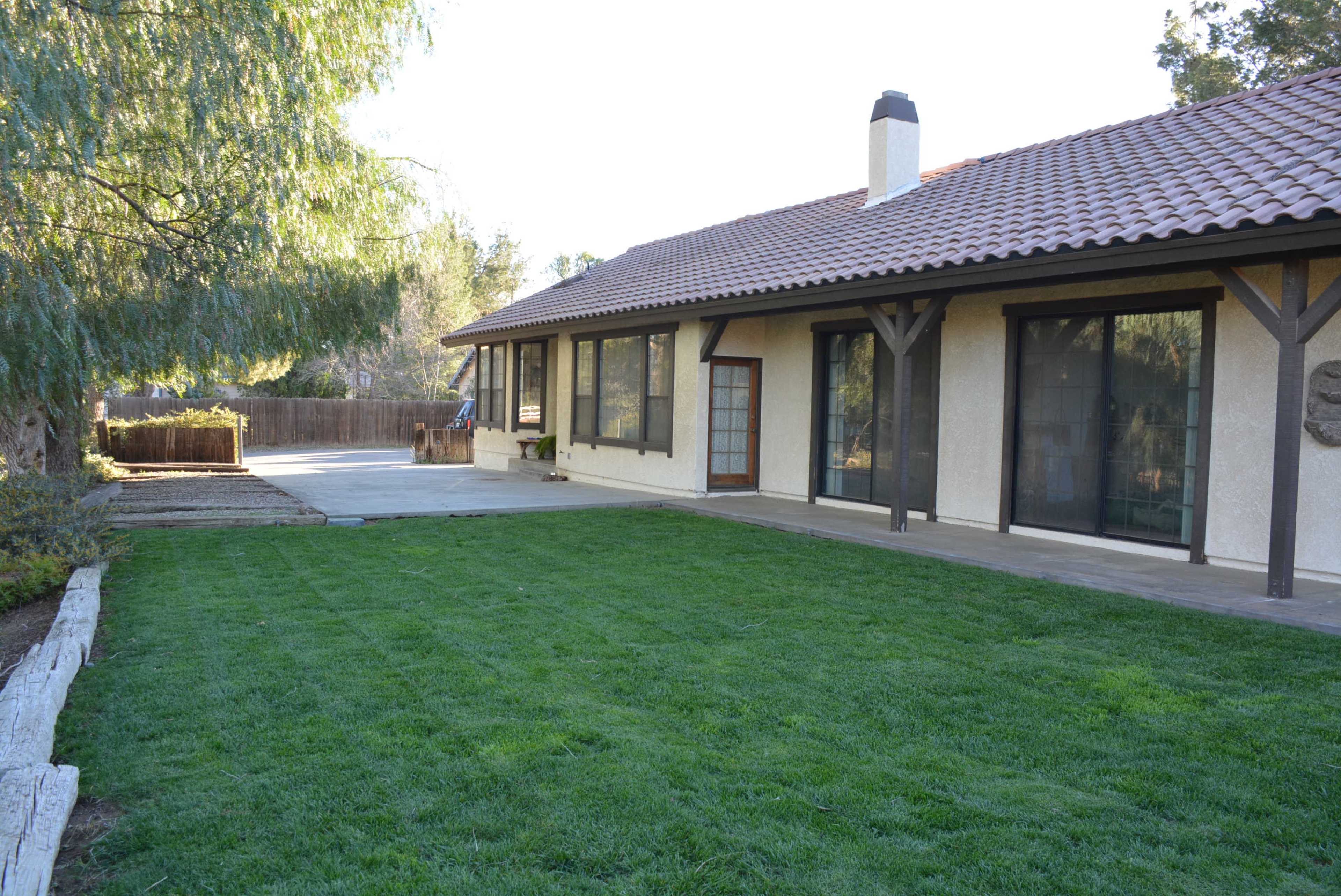 The image shows a single-story house with a tiled roof and a landscaped backyard featuring freshly cut grass.