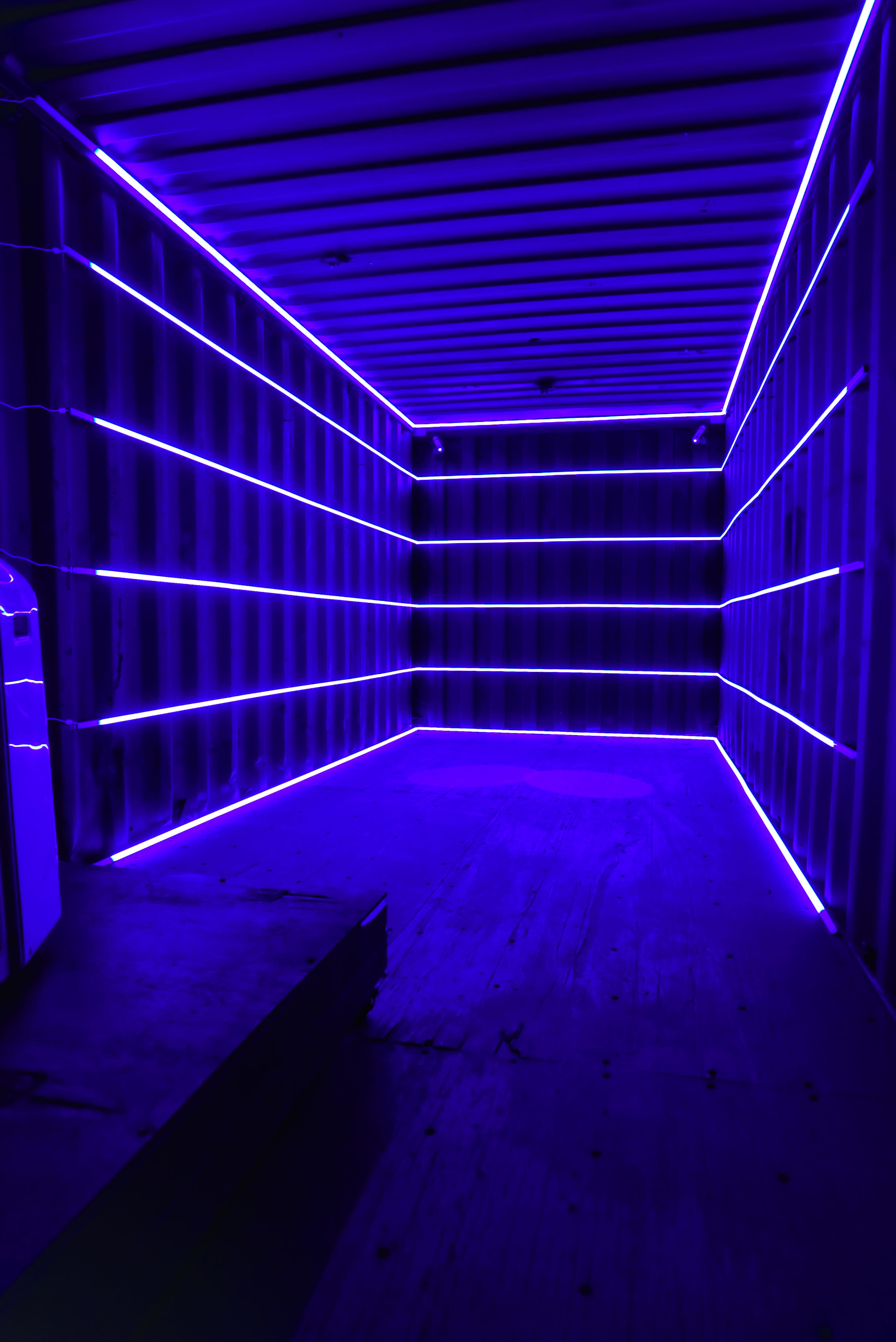 The image shows the interior of a shipping container illuminated by purple LED lights along the walls.