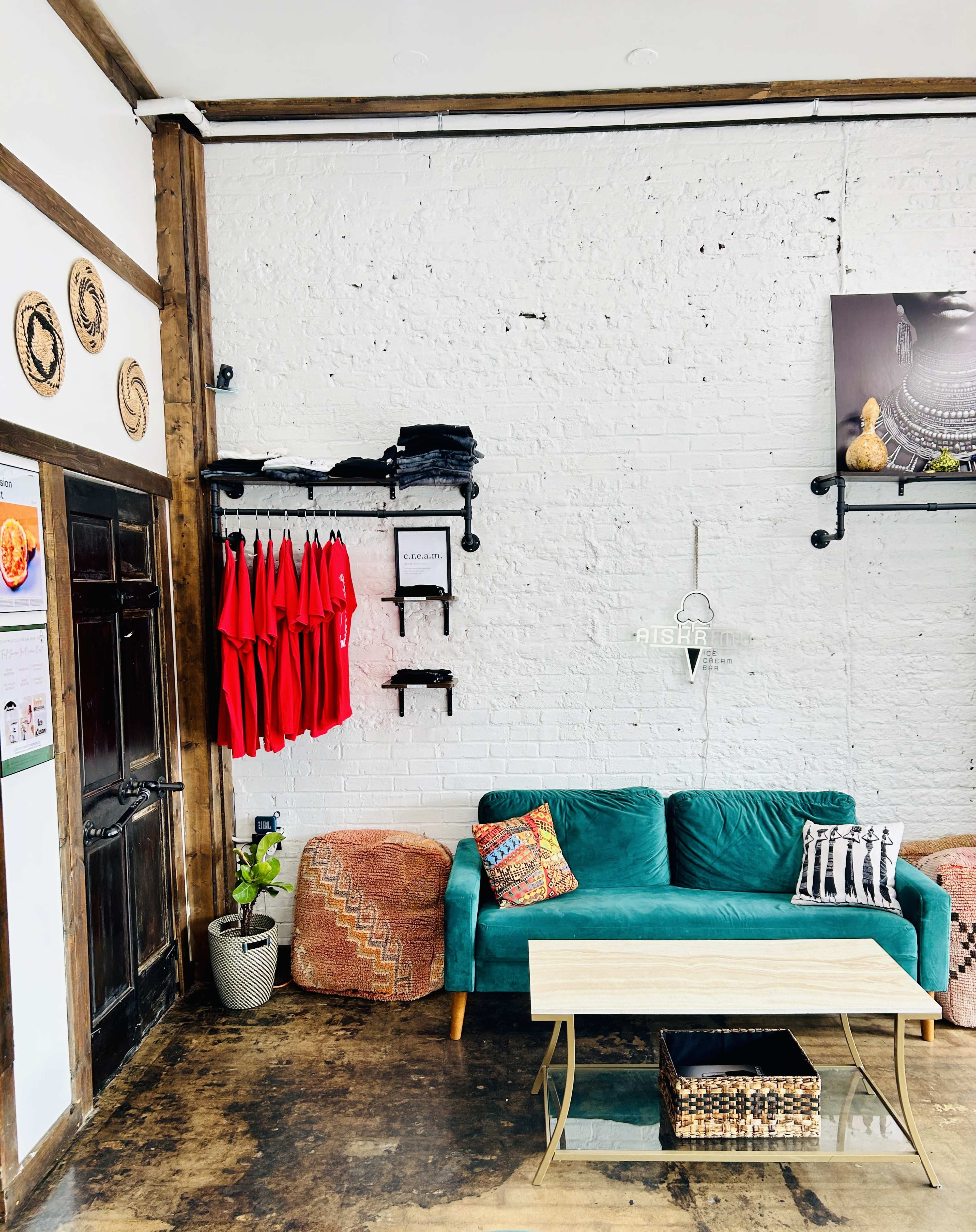 The image features a cozy lounge area with a green sofa, a wooden coffee table, and red aprons hanging on the wall in a well-lit space.