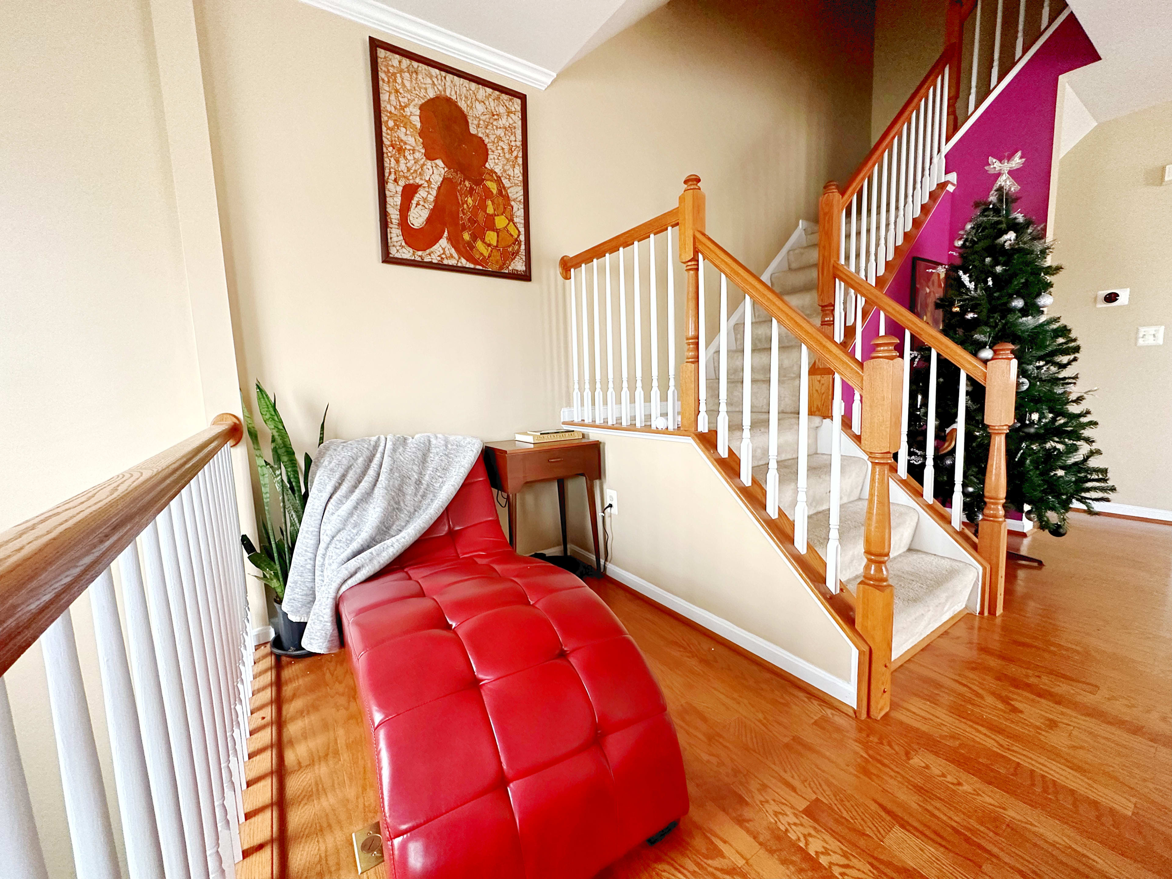 A foyer with a red tufted bench, a small side table, an indoor plant, a staircase leading to the upper level, and a decorated Christmas tree in the corner.