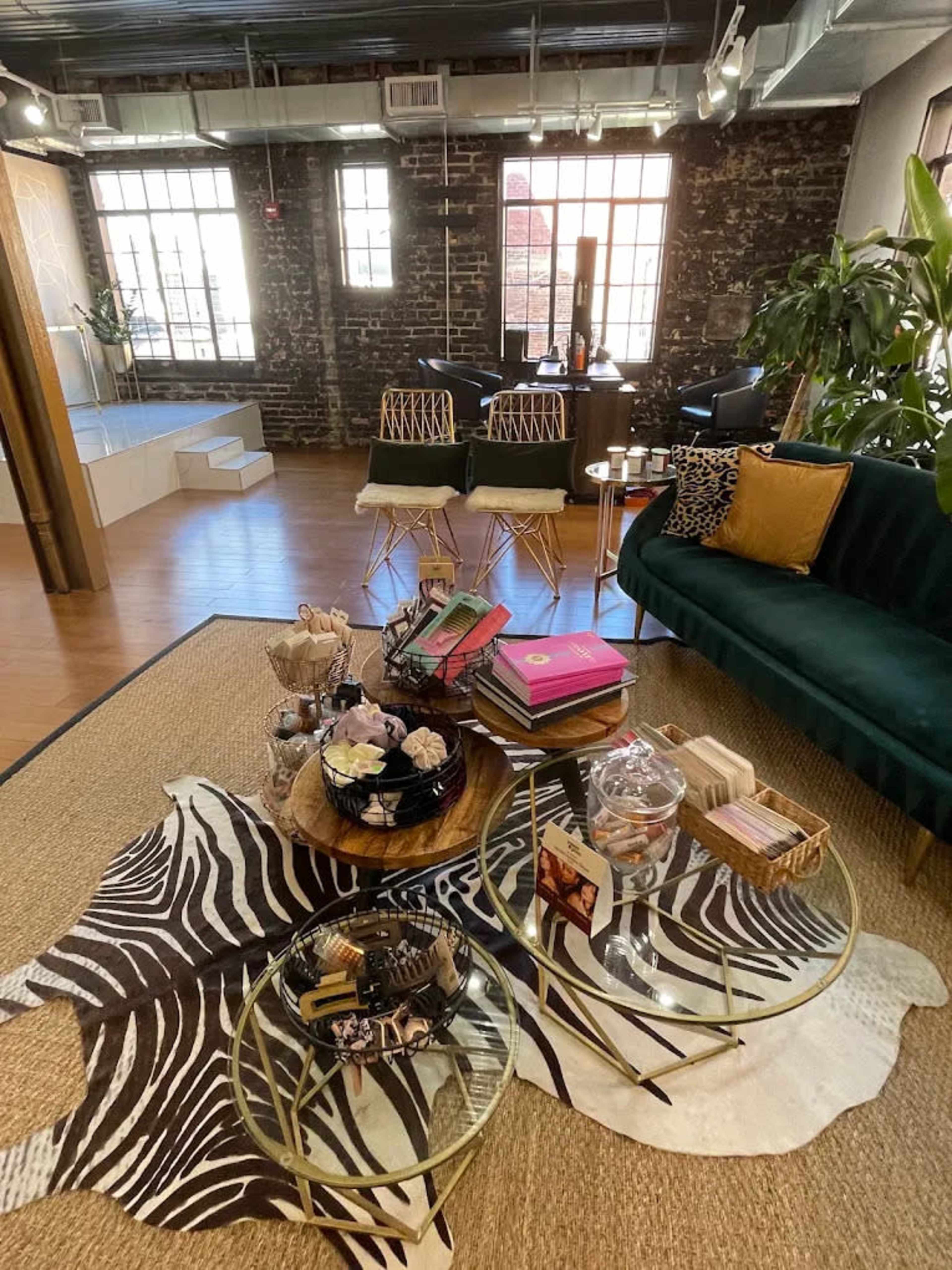 The image shows a stylish interior featuring a green velvet sofa, a zebra-print rug, circular coffee tables, and various decorative items arranged on the floor.