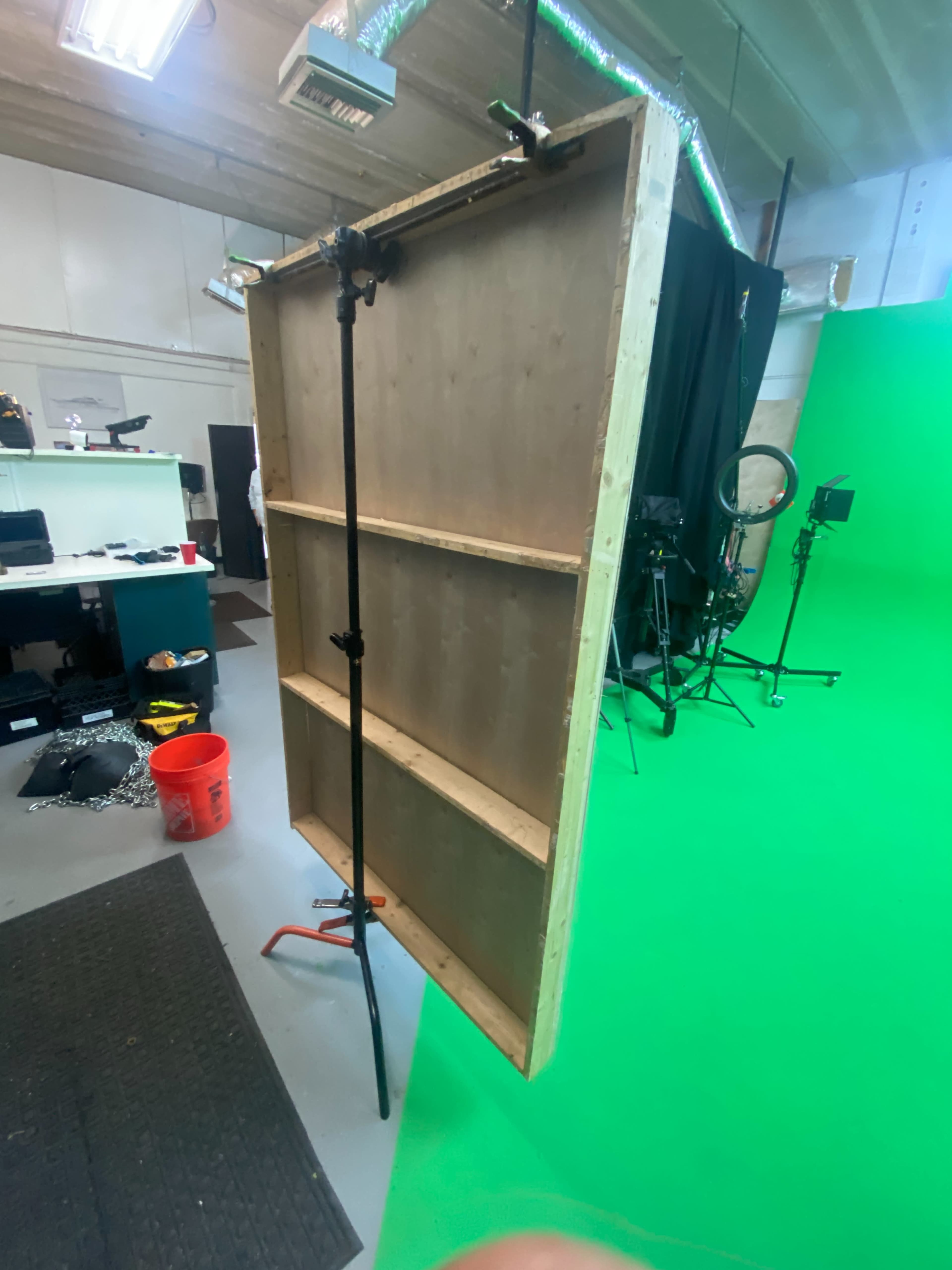 A large wooden panel mounted on a stand, with a green backdrop and various studio equipment in the background.