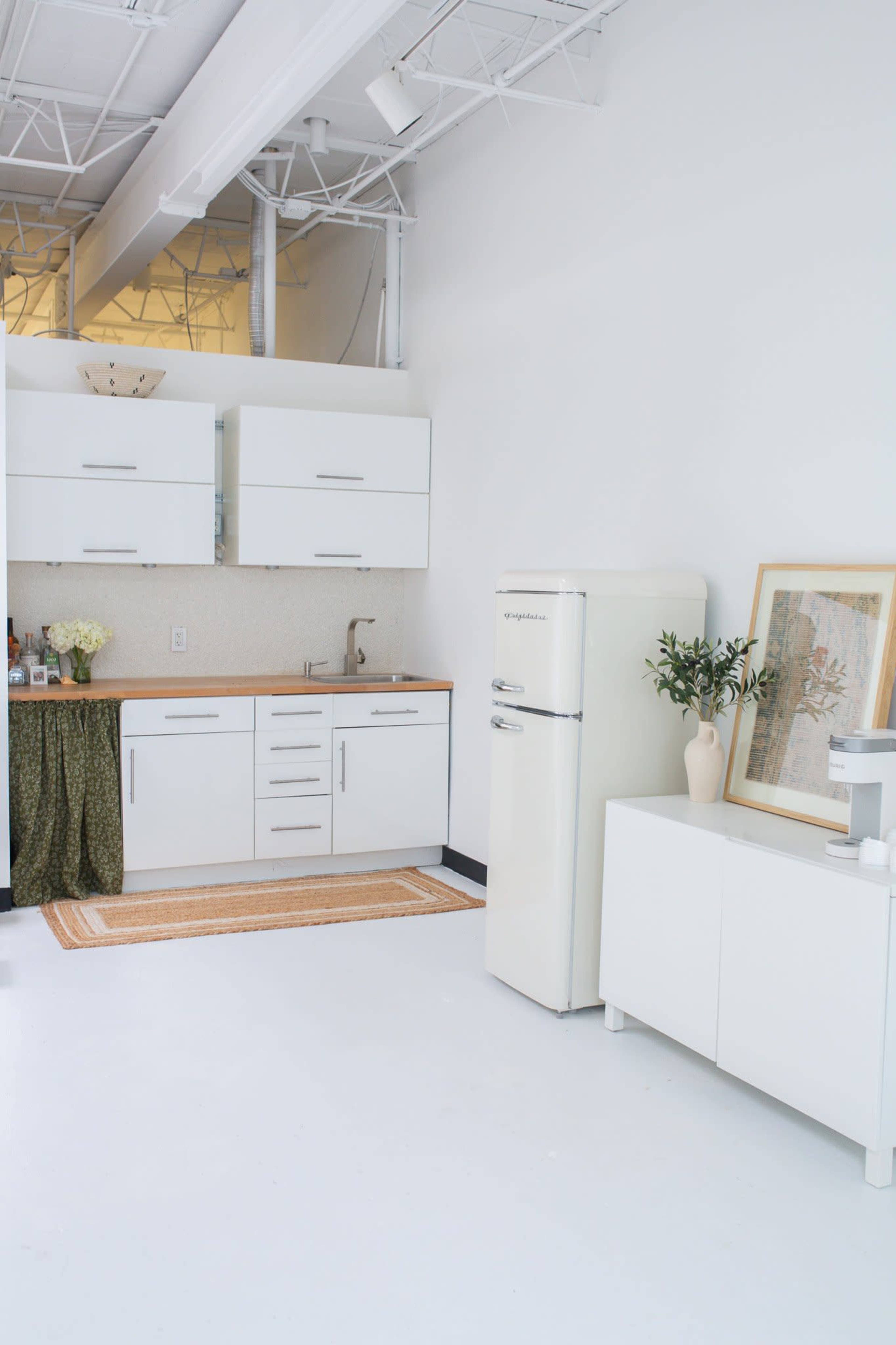 The image shows a modern kitchen with white cabinetry, a wooden countertop, a retro-style cream refrigerator, and decorative elements on the walls and countertop.