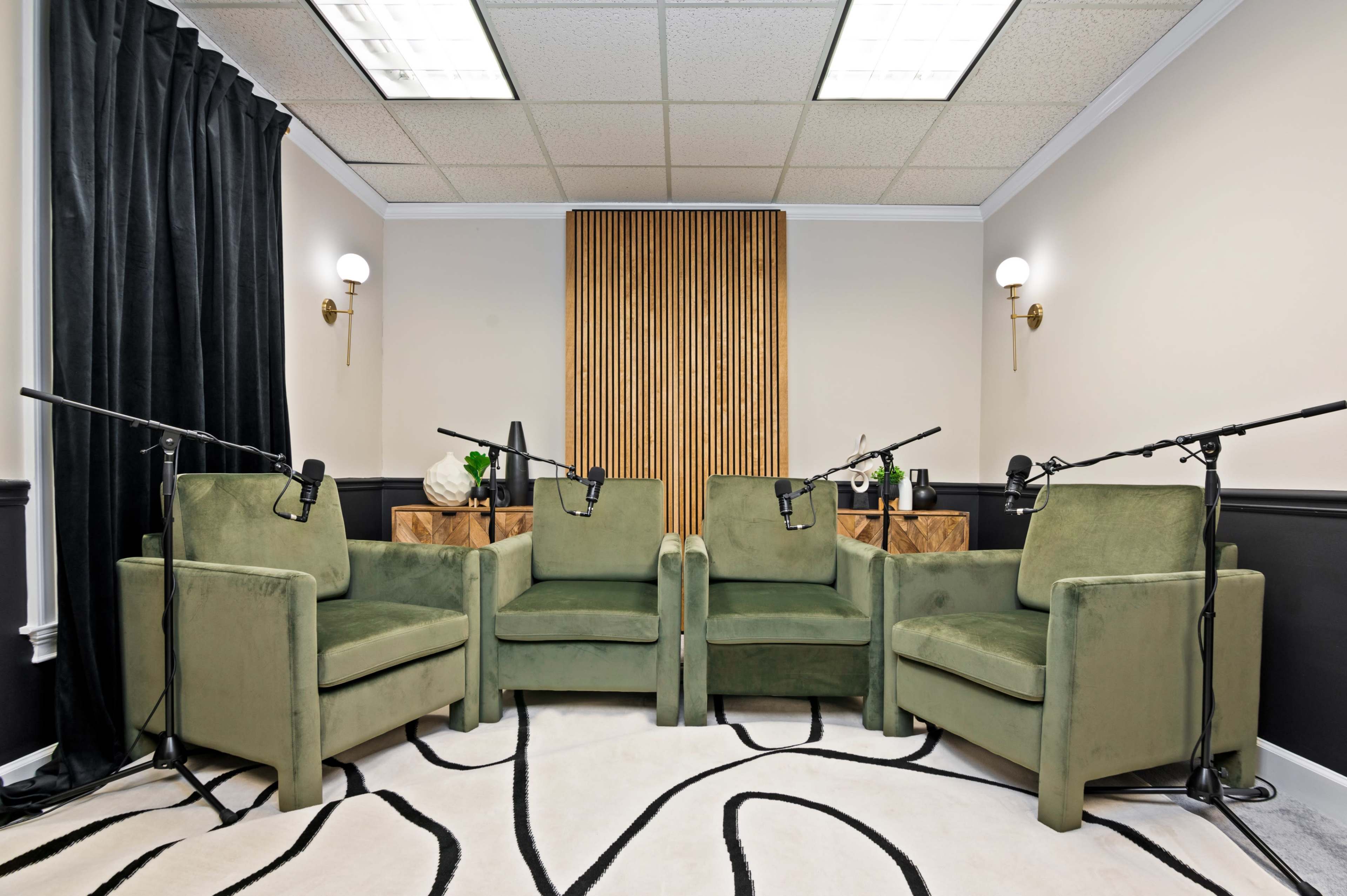 A recording studio features four green chairs arranged around a central space, with microphones positioned on stands in front of each chair.