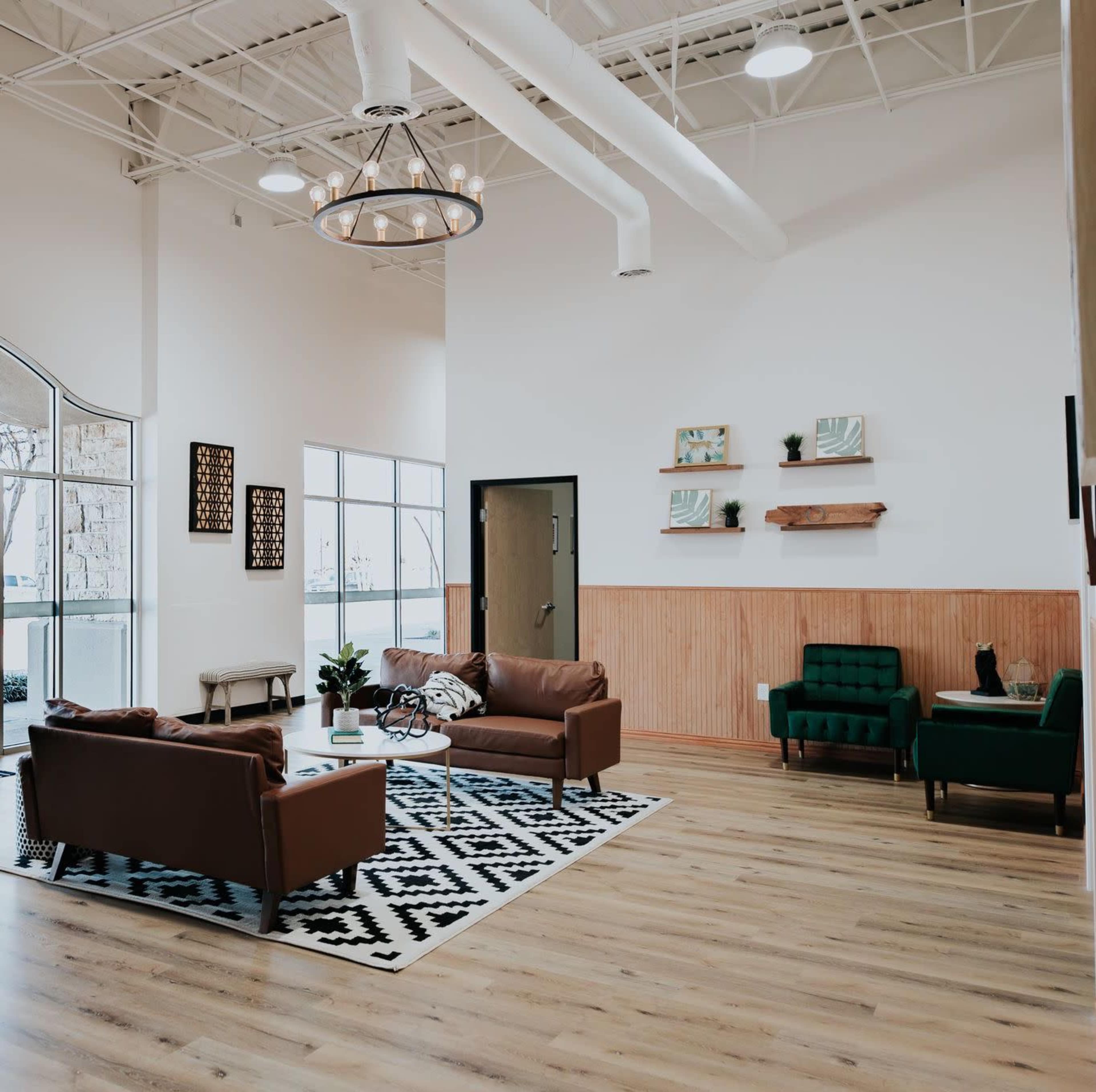 The image shows a modern lounge area with brown leather sofas, green armchairs, a patterned rug, and wooden wall accents.