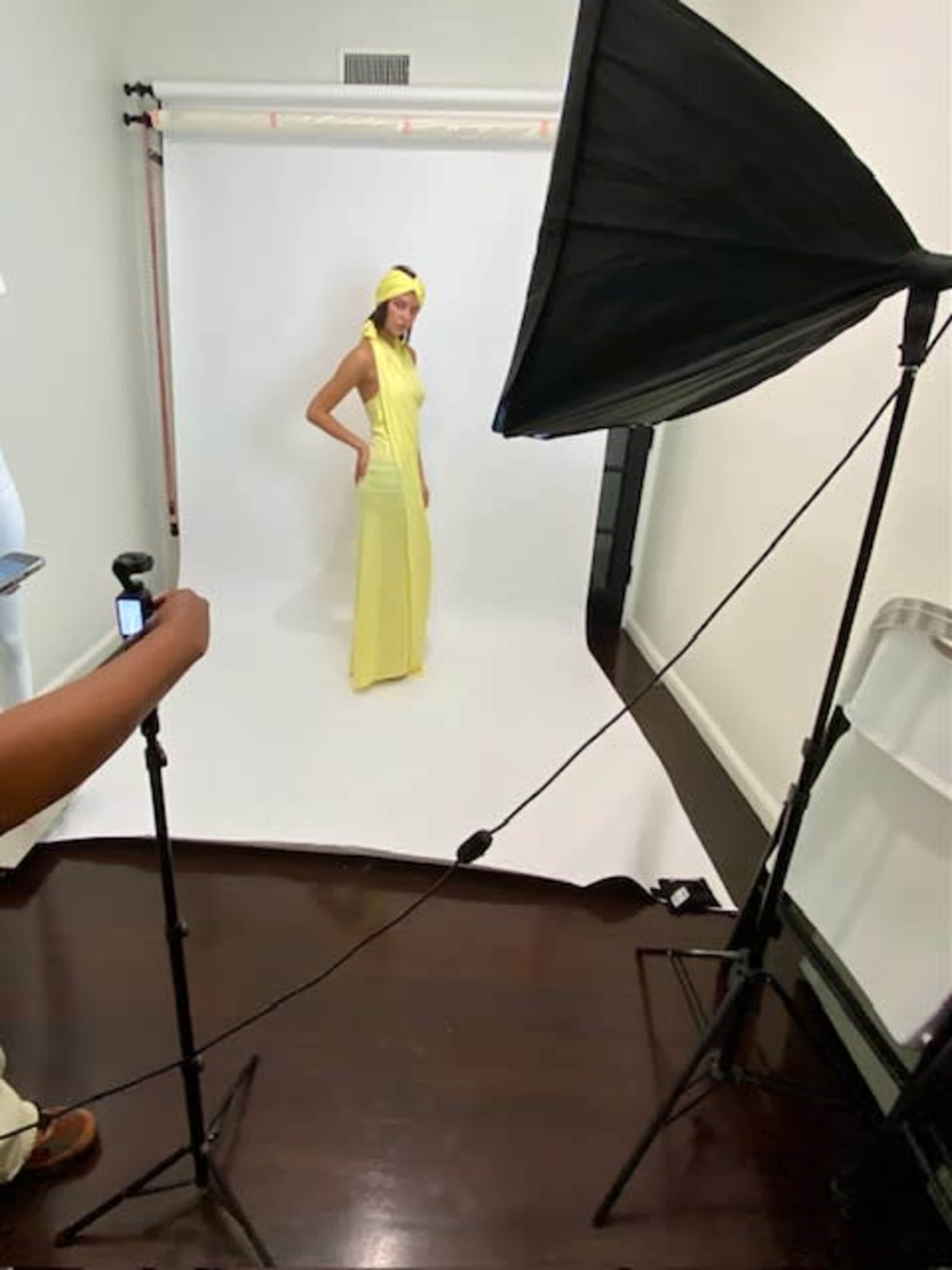 A model poses in a yellow dress in a studio setting with softbox lighting and a white backdrop.