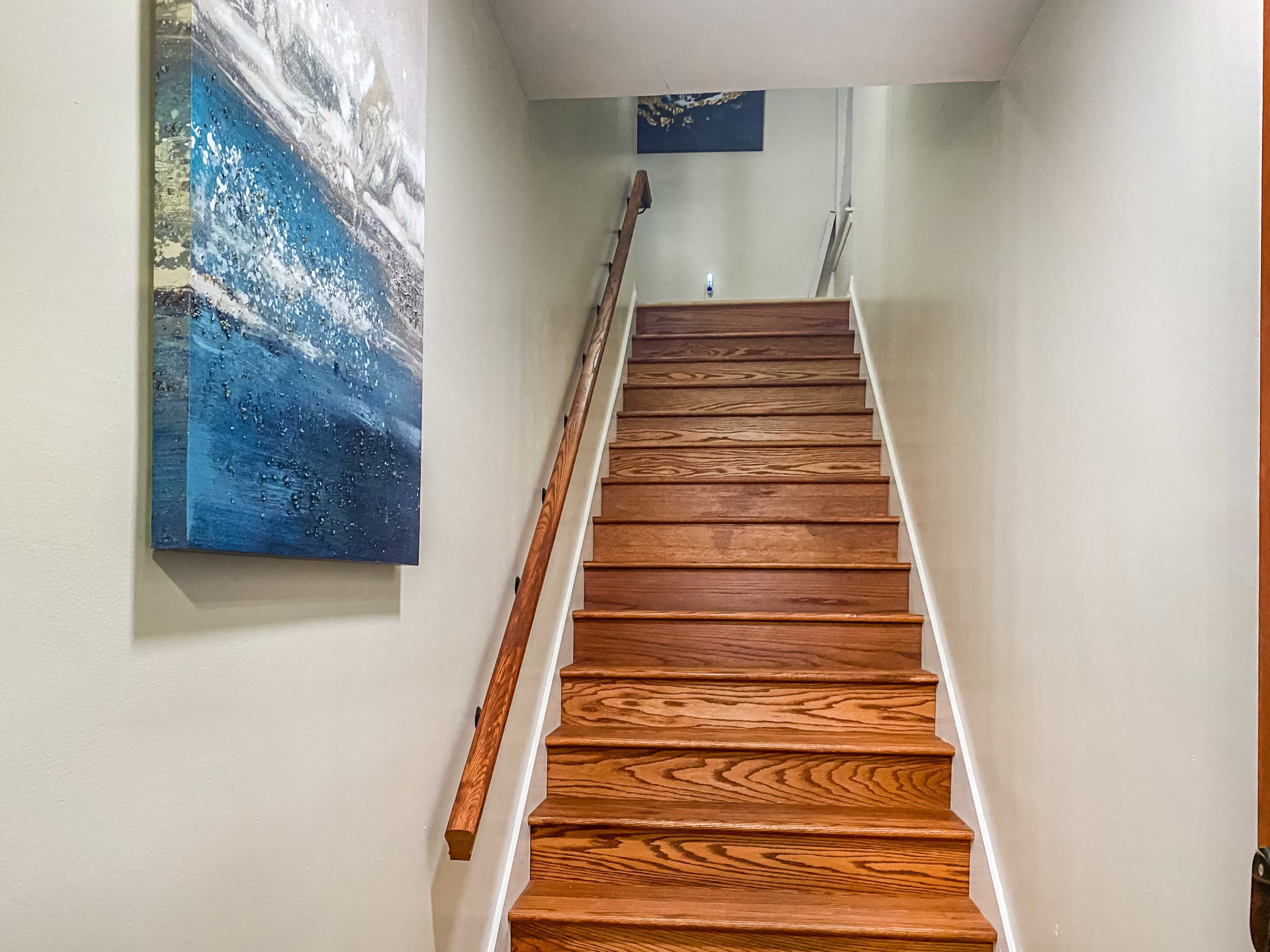 A set of wooden stairs leads upward, flanked by a wall with a painting featuring blue hues.