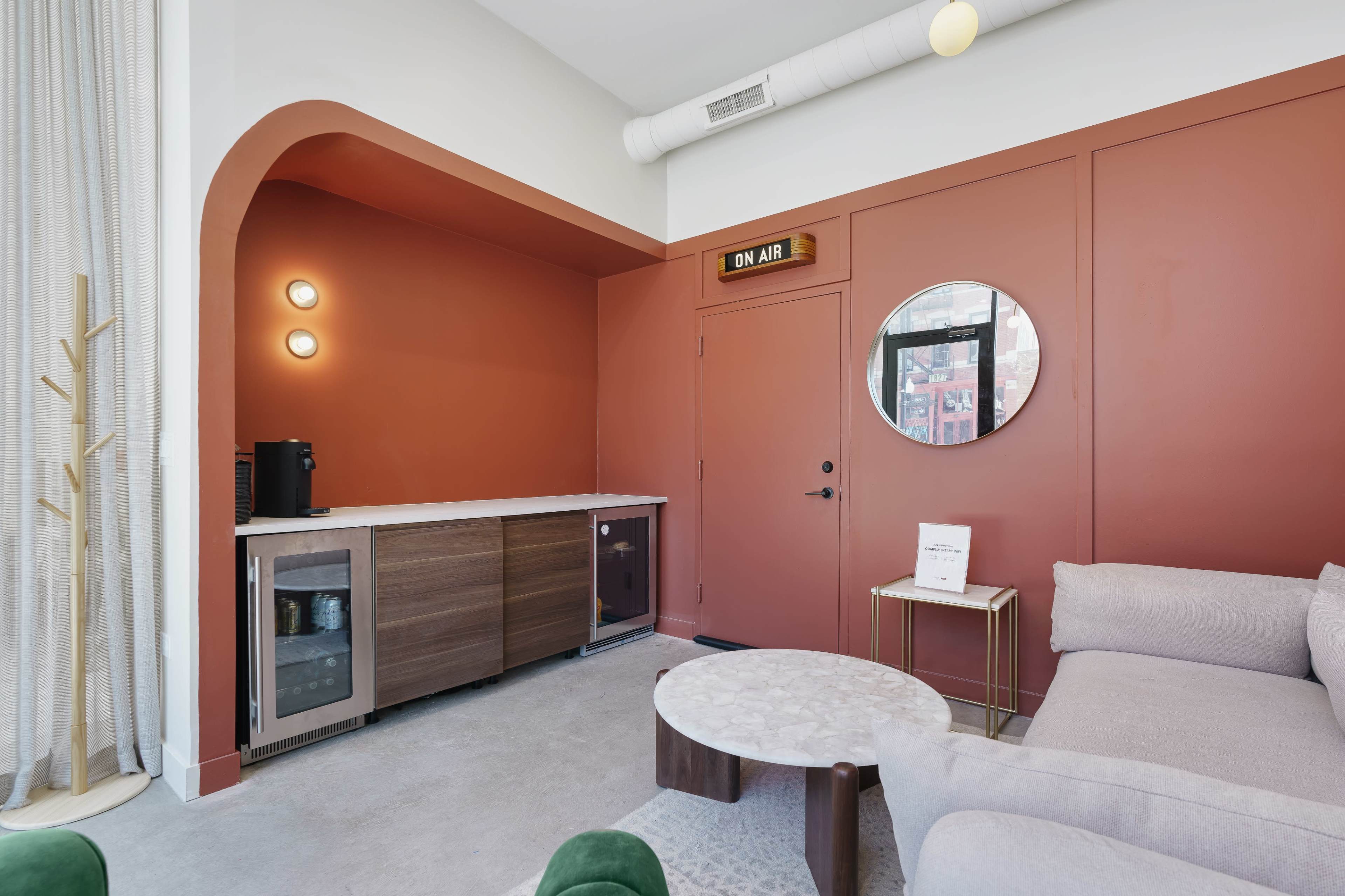 A modern interior featuring a coffee station with a dark wooden countertop, a round mirror on the wall, and a light gray sofa in a room with a warm-colored accent wall.