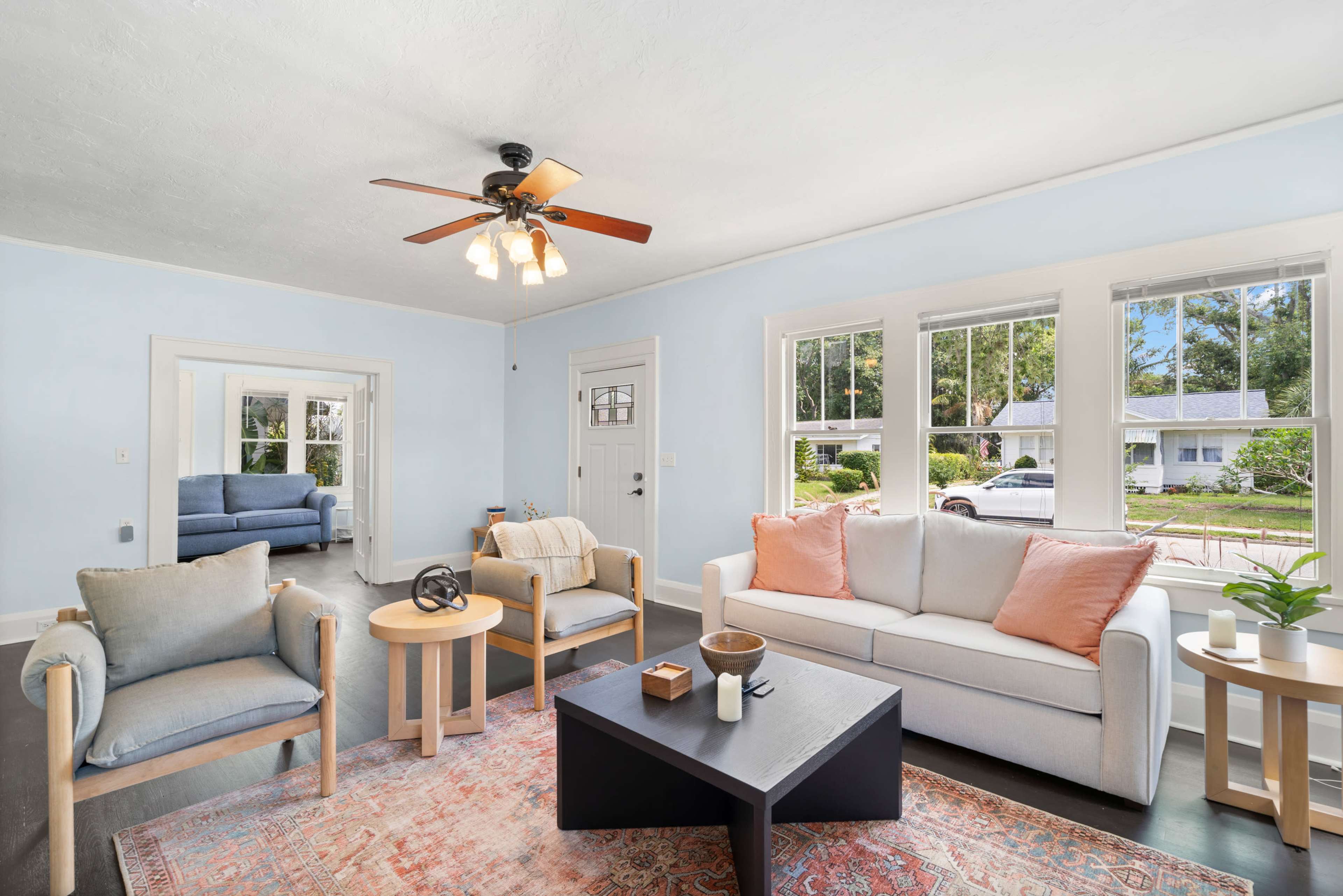 A bright living room features a light blue color scheme, a comfortable sofa, armchairs, and large windows letting in natural light.