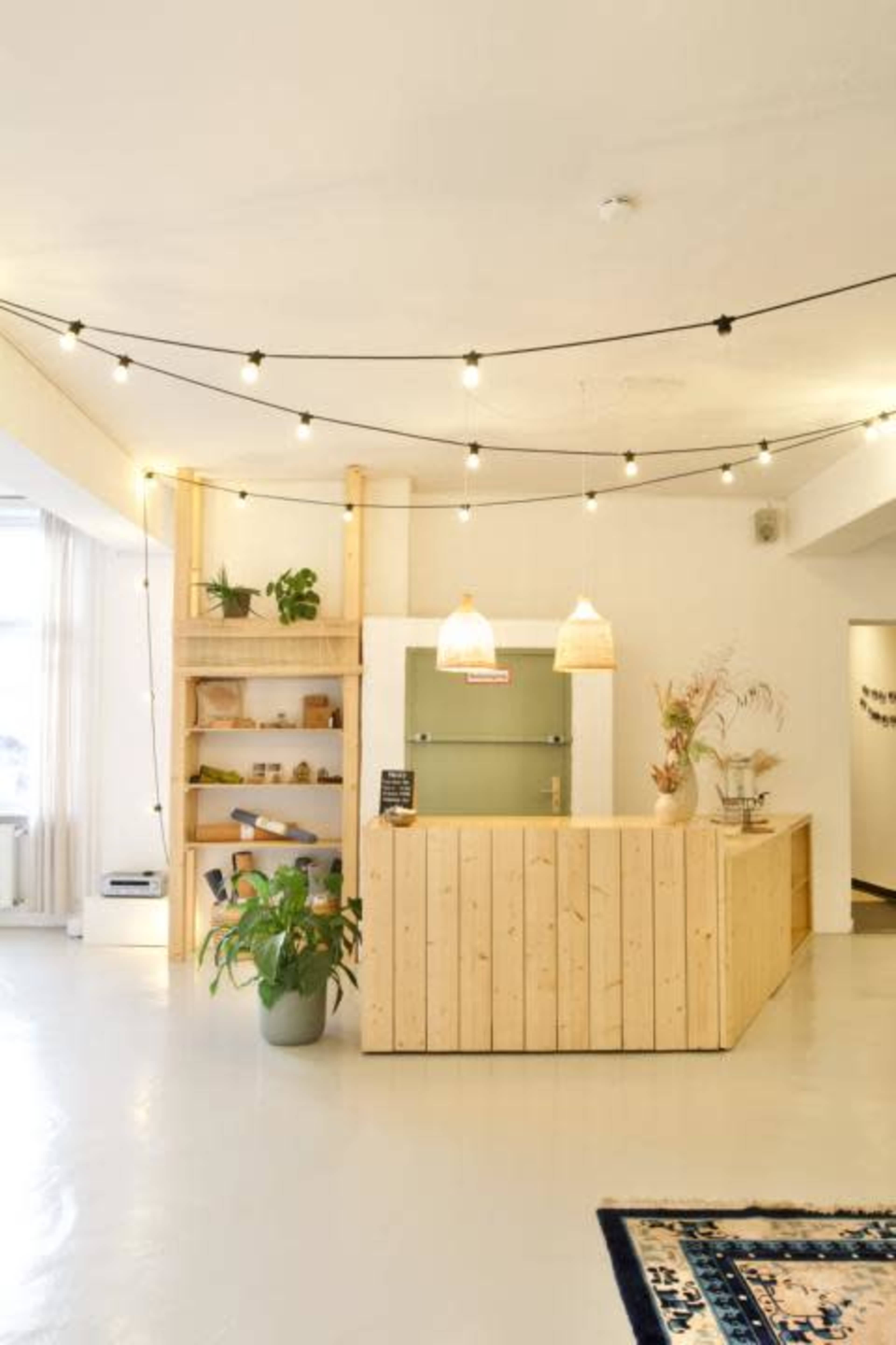 A reception area with a wooden front desk, hanging light fixtures, shelves with plants, and a minimalist design.