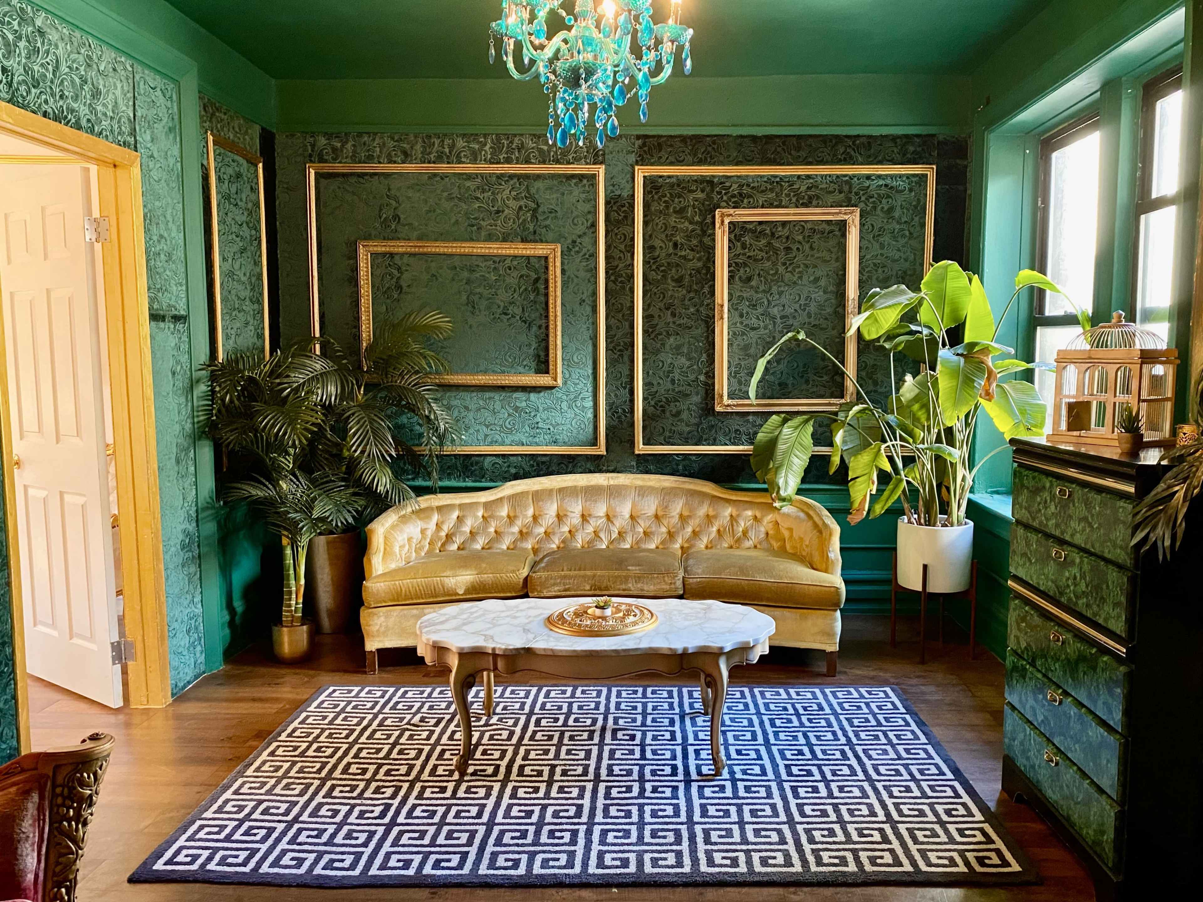 A vintage living room with green wallpaper, a gold tufted sofa, a coffee table, and decorative plants.