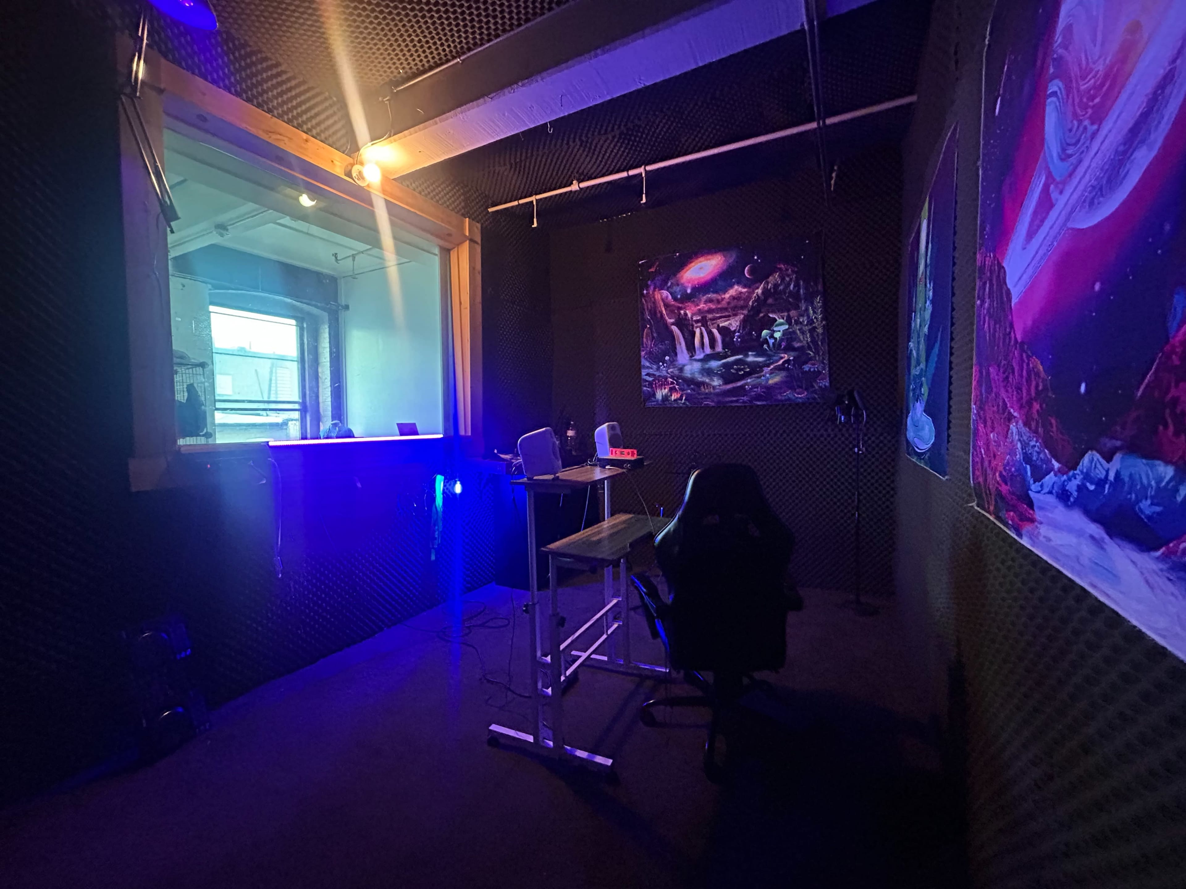 The image shows a soundproof recording studio with a desk, chair, and colorful wall art.