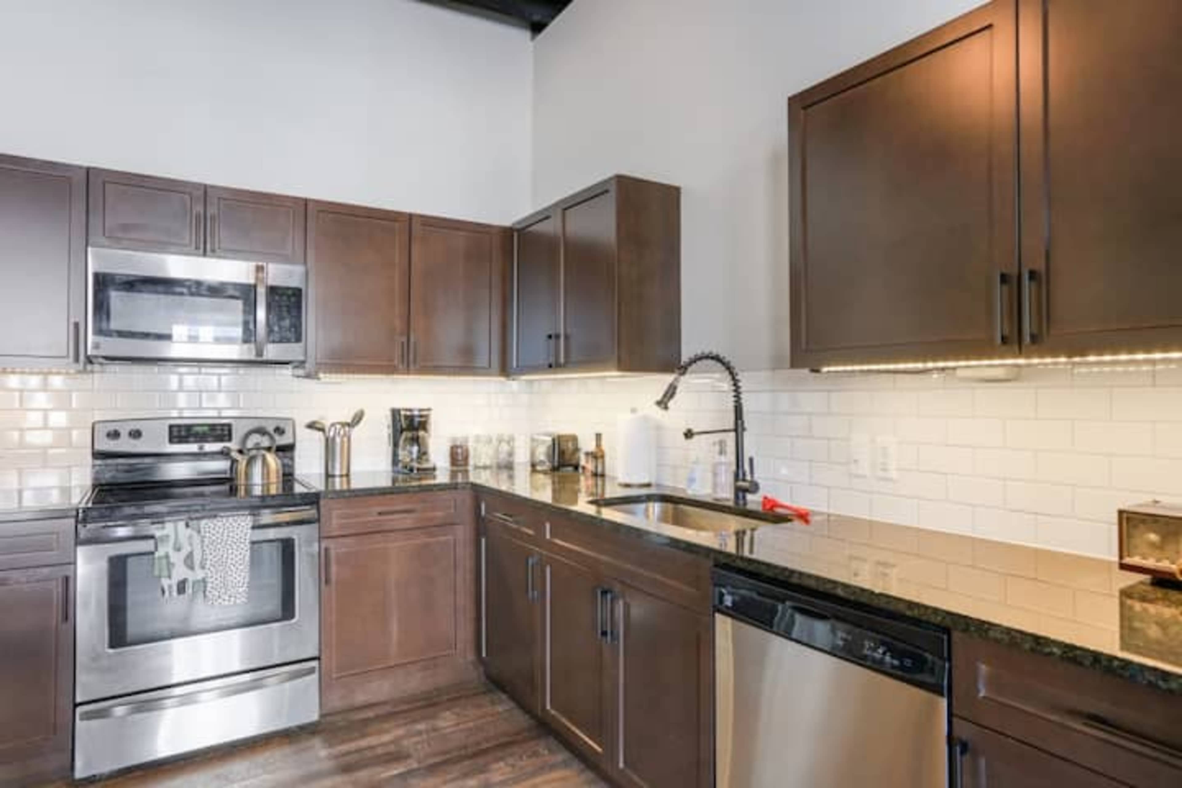 The kitchen features dark wood cabinetry, stainless steel appliances, and a black granite countertop with a tile backsplash.
