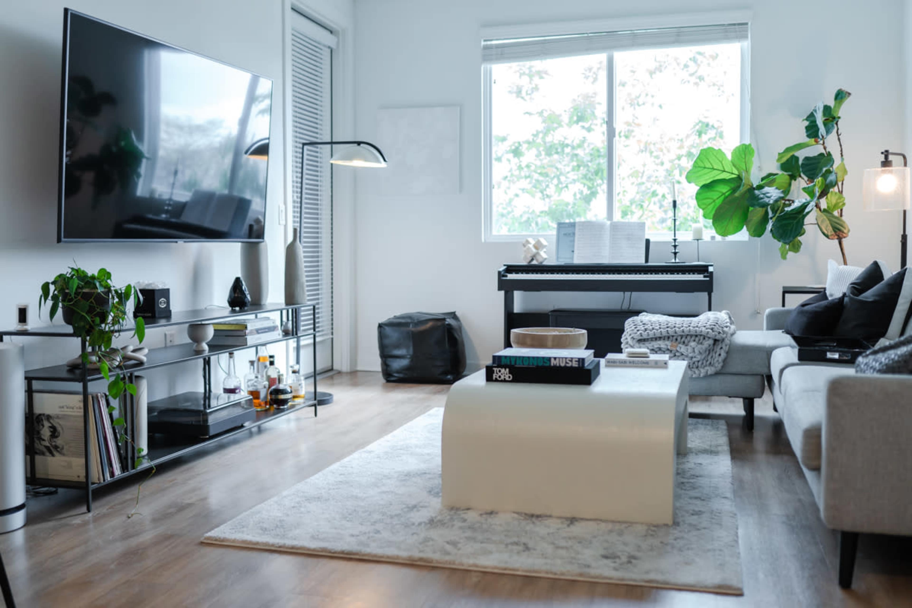 A modern living room with a television, a piano, a couch, and a coffee table on a light-colored rug.