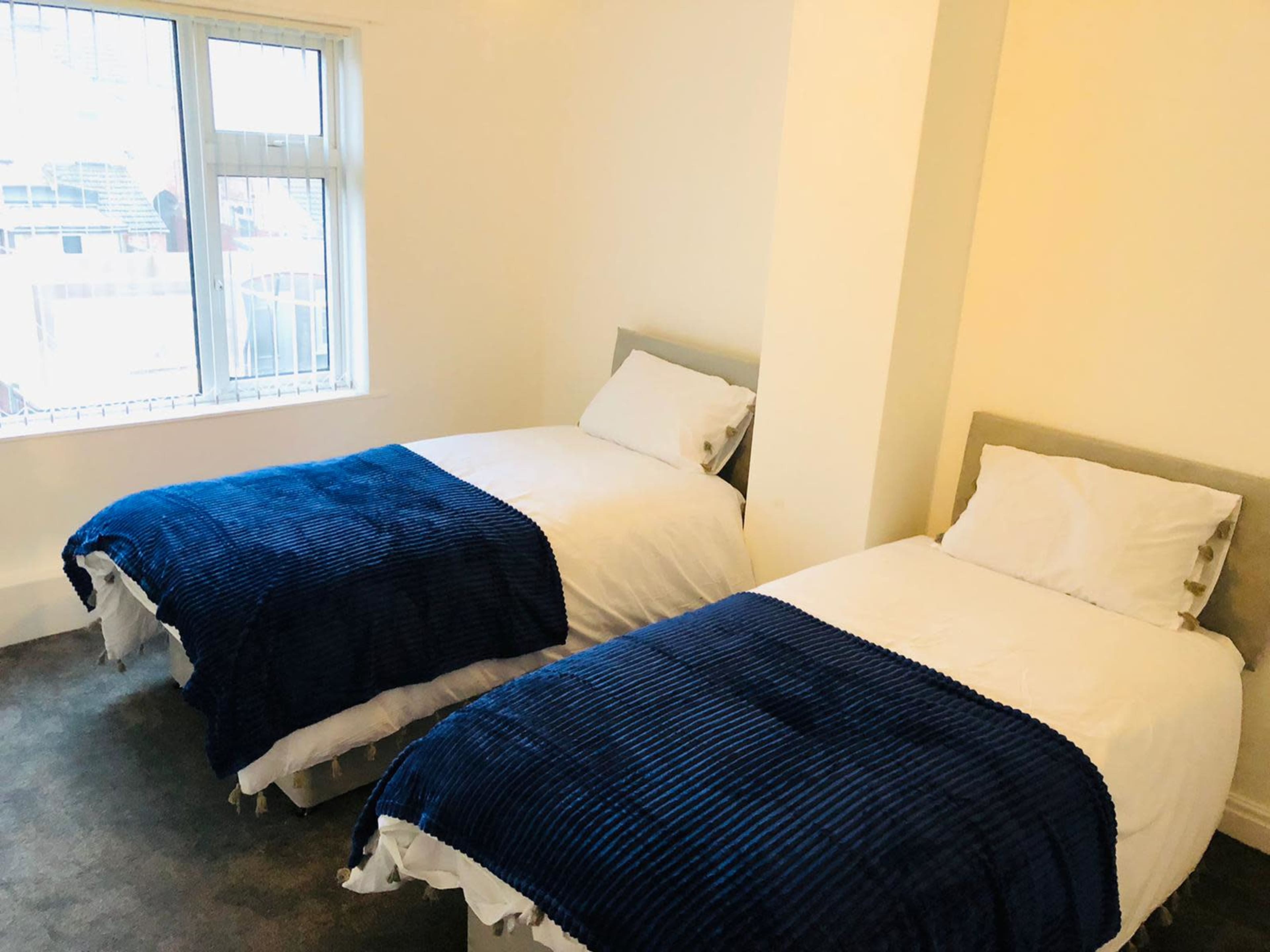 A room with two twin beds covered with blue blankets and a window letting in natural light.