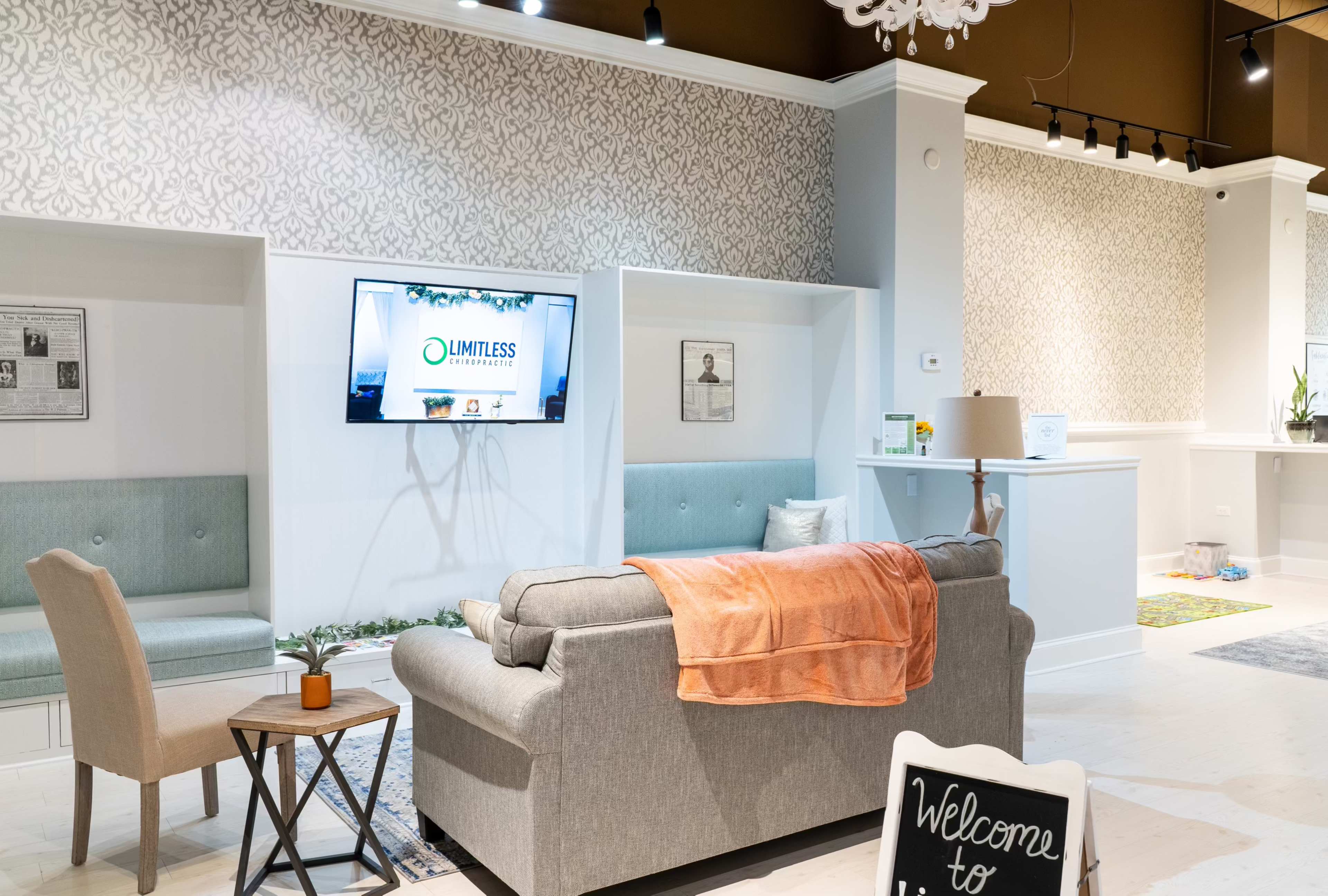 A modern lounge area features a gray sofa with an orange throw, two seating spaces, and a television mounted on the wall.