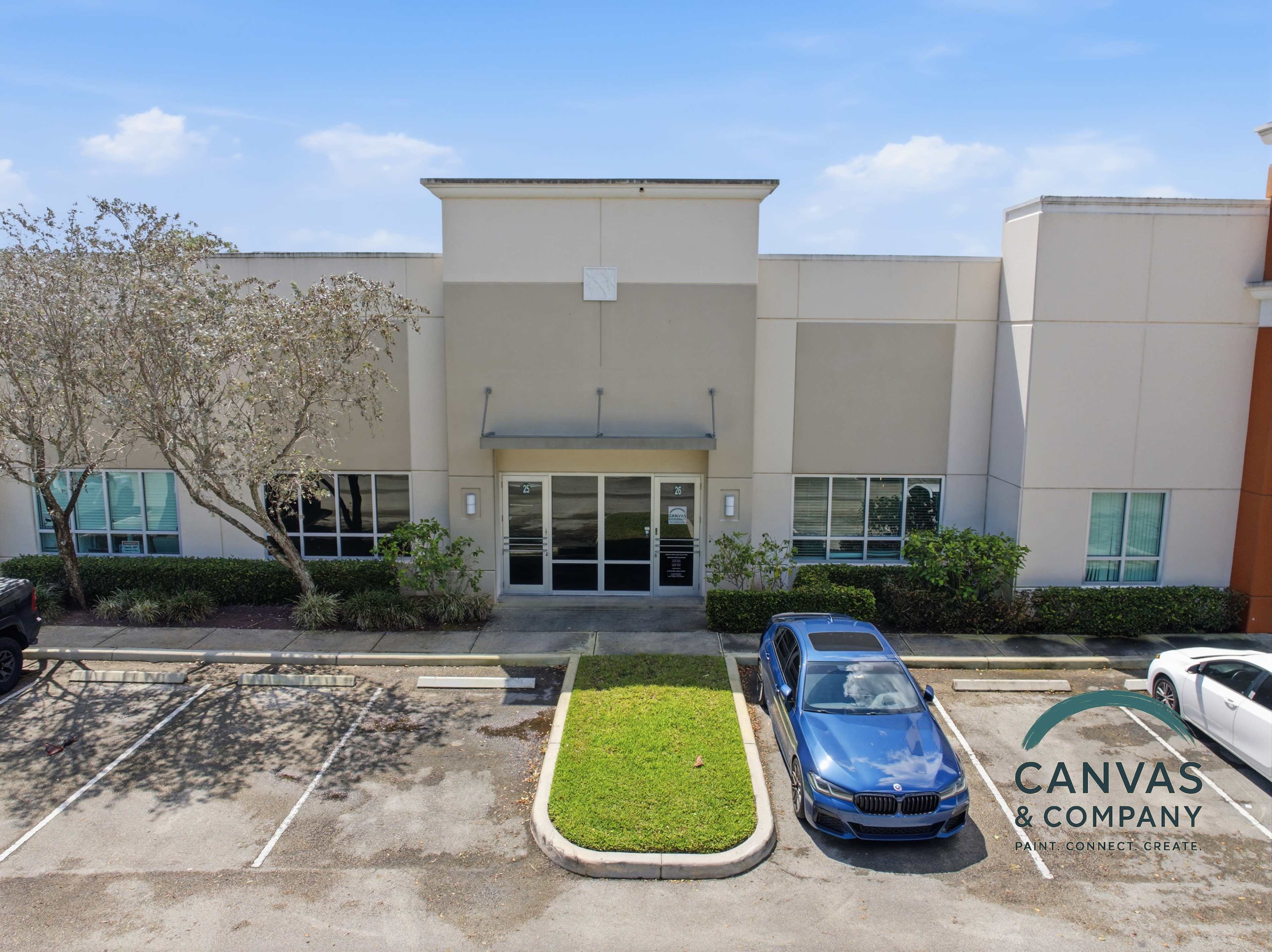 The image shows the exterior of a commercial building with large glass windows, a canopy entrance, and a parked blue car in the foreground.