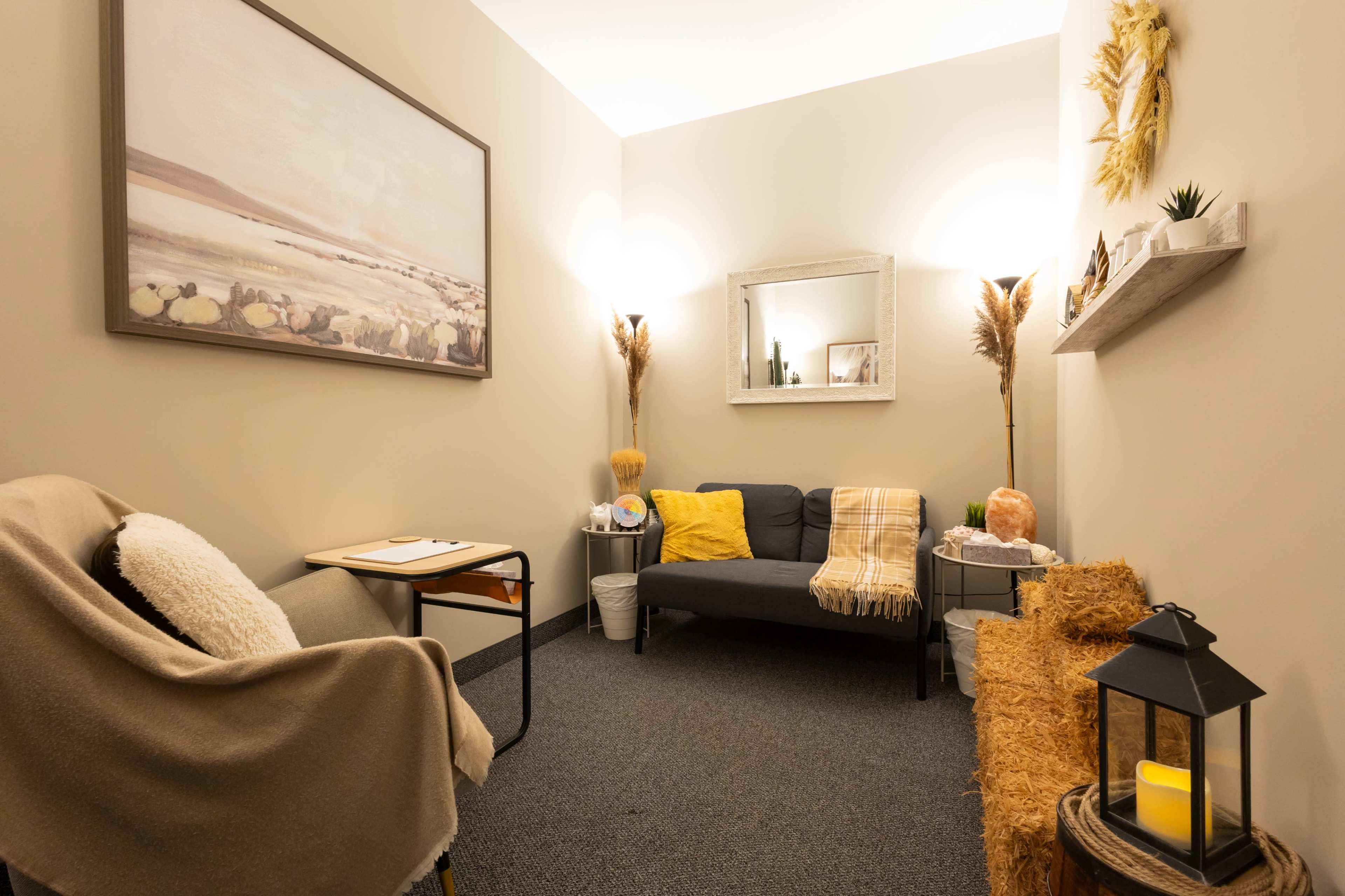 The image shows a cozy room furnished with a dark sofa, a small table, a decorative shelf, and warm lighting.