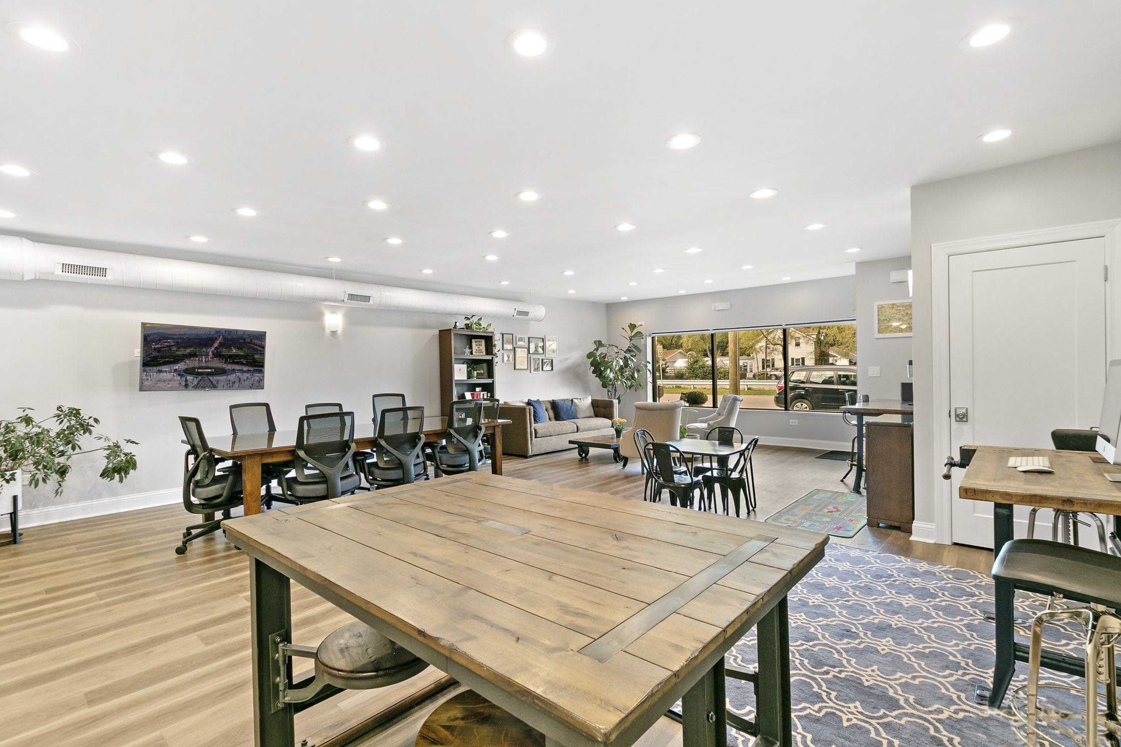 A modern office space with multiple workstations, a lounge area, and large windows providing natural light.