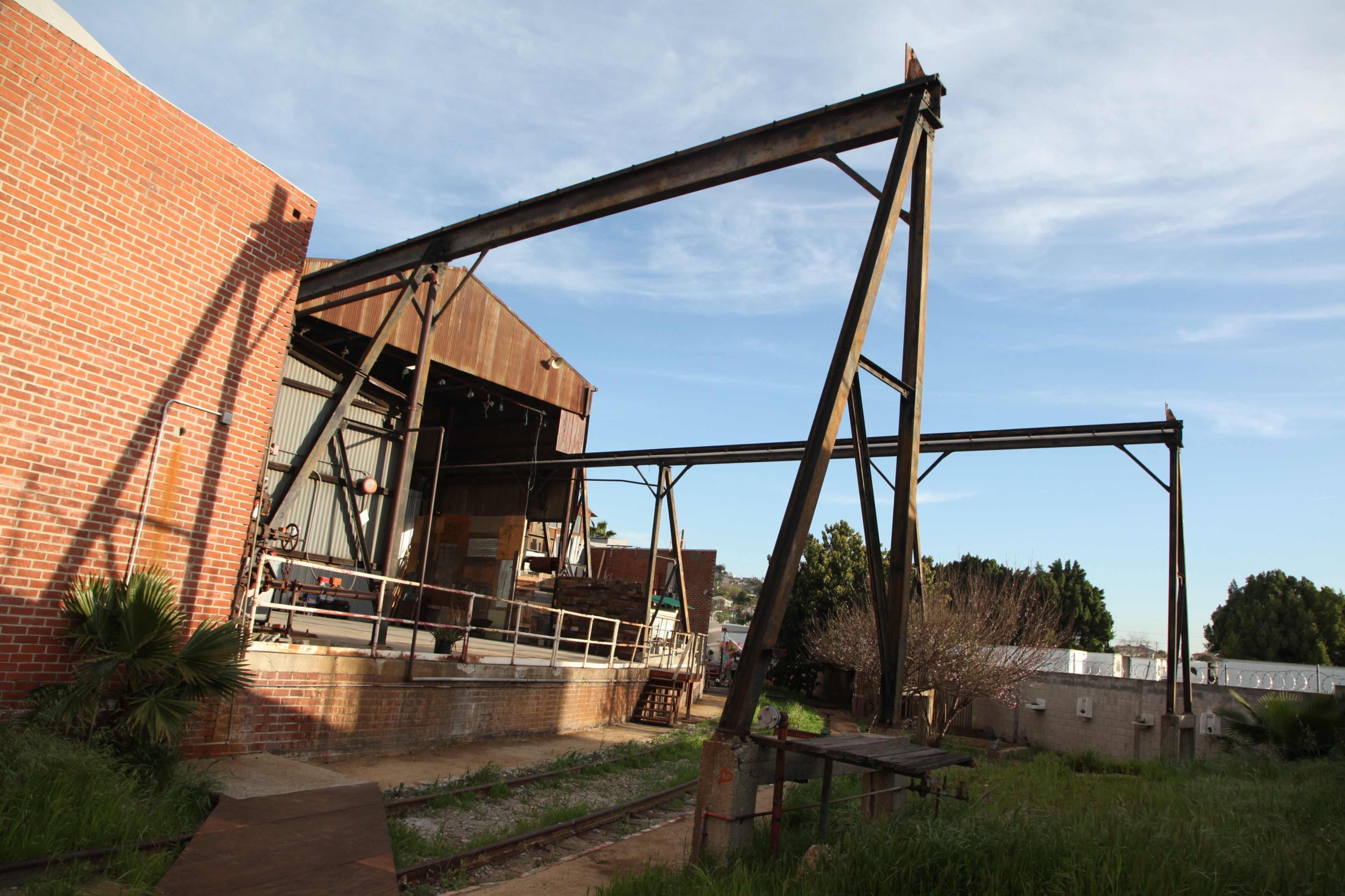 A rusted steel framework stands next to a brick building, partially covered in greenery.