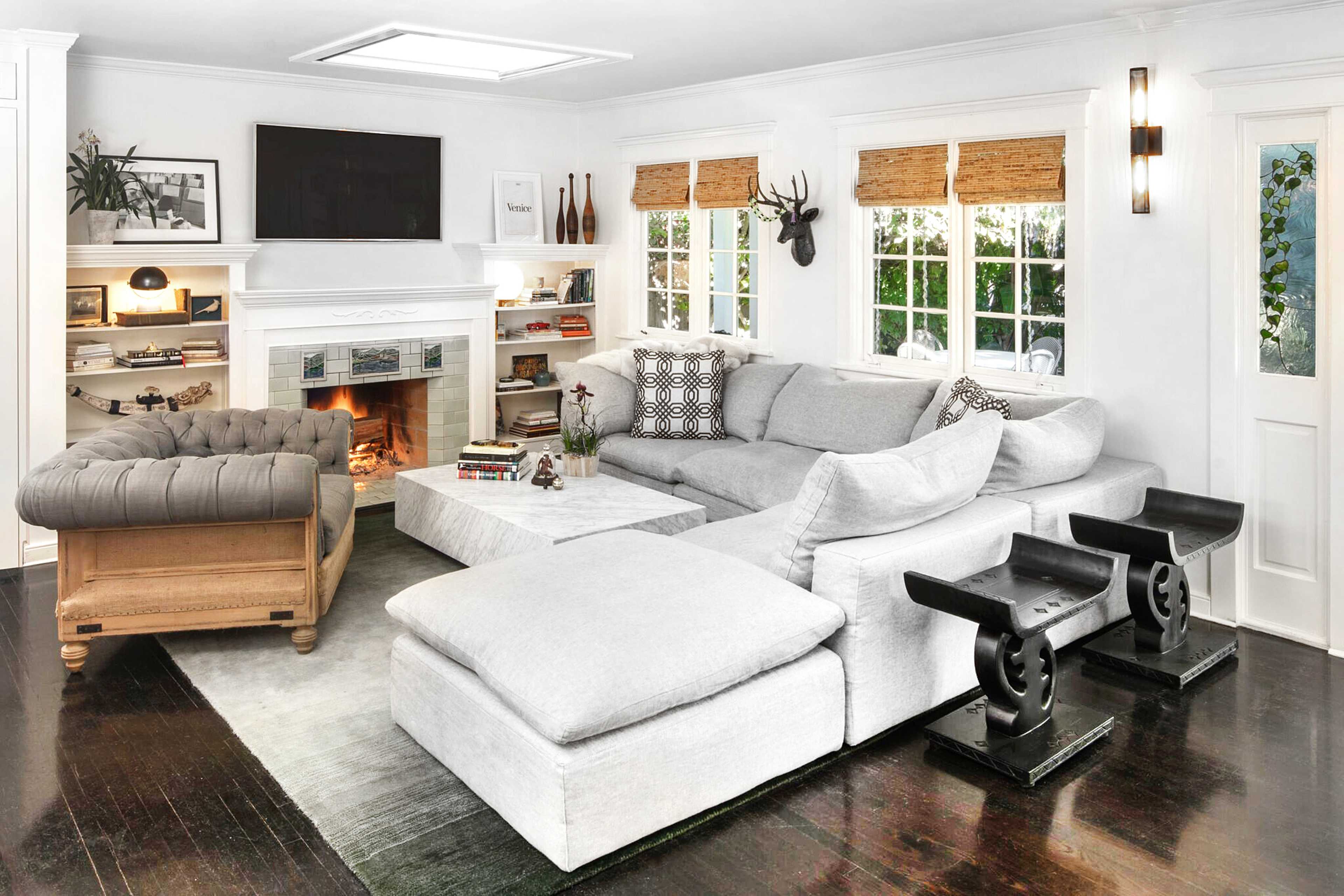 A cozy living room featuring a large gray sectional sofa, a fireplace with a TV above it, and bookshelves filled with decorative items.