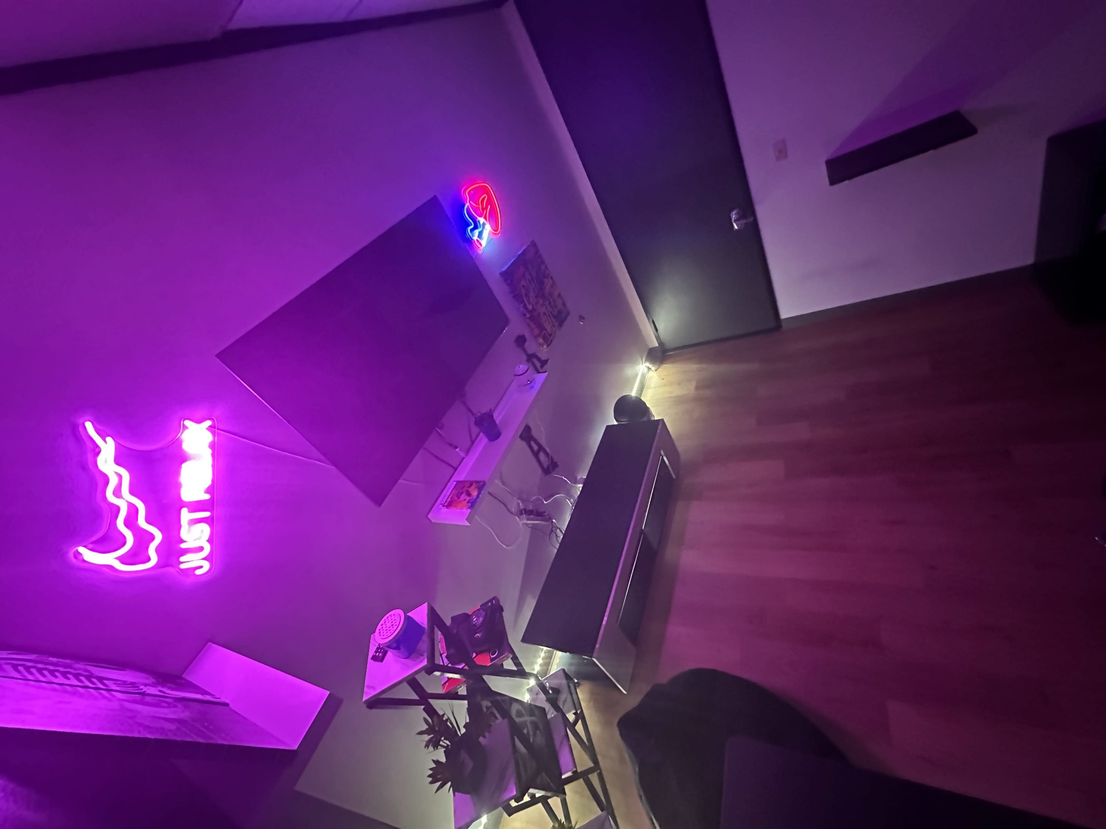 A modern living room with a wall-mounted television, a sleek entertainment unit, neon signage, and wooden flooring.