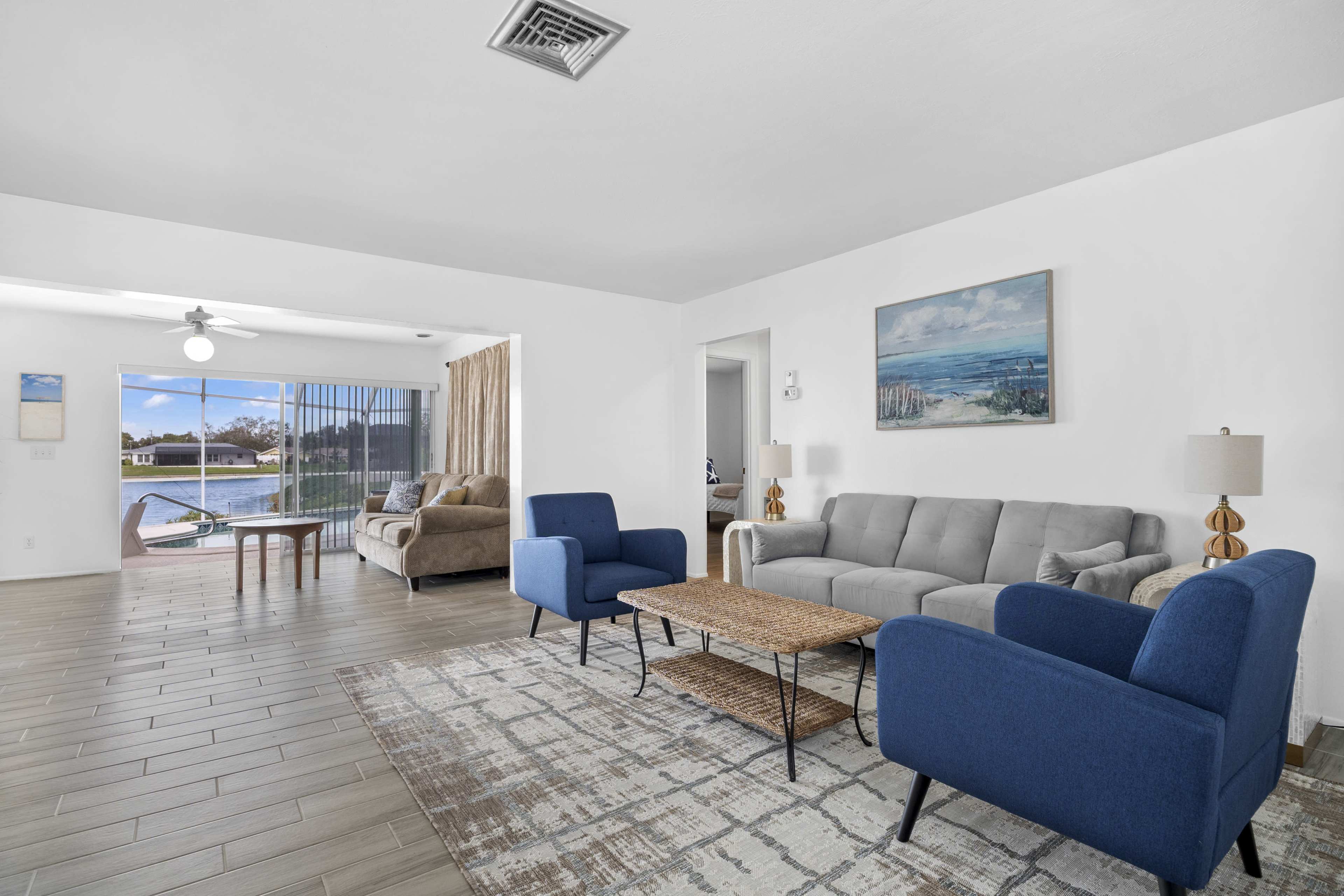 A living room with a gray sofa, blue chairs, a wooden coffee table, and large windows overlooking a pool area.