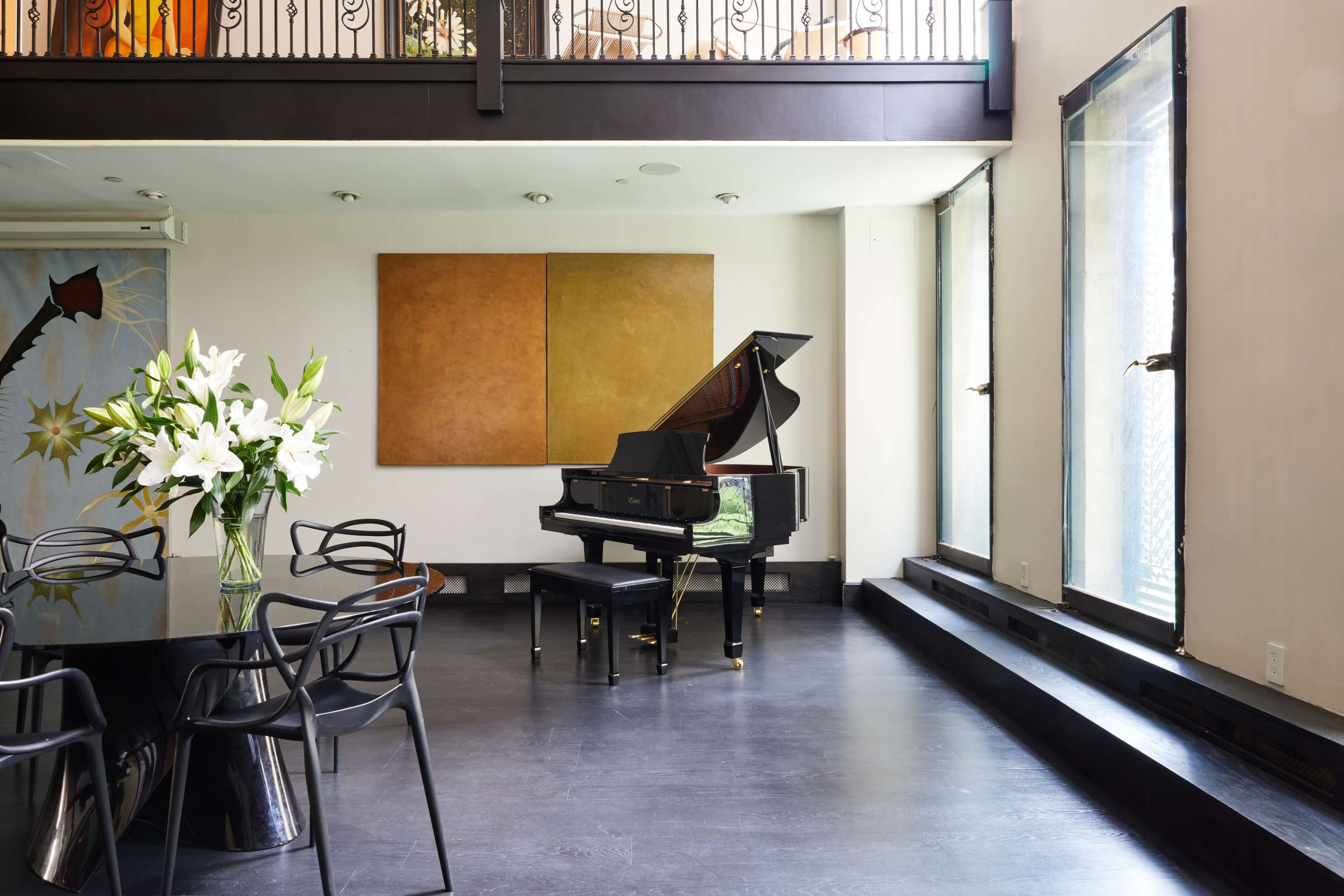 A grand piano sits in the corner of a spacious room featuring large windows and minimalist decor.