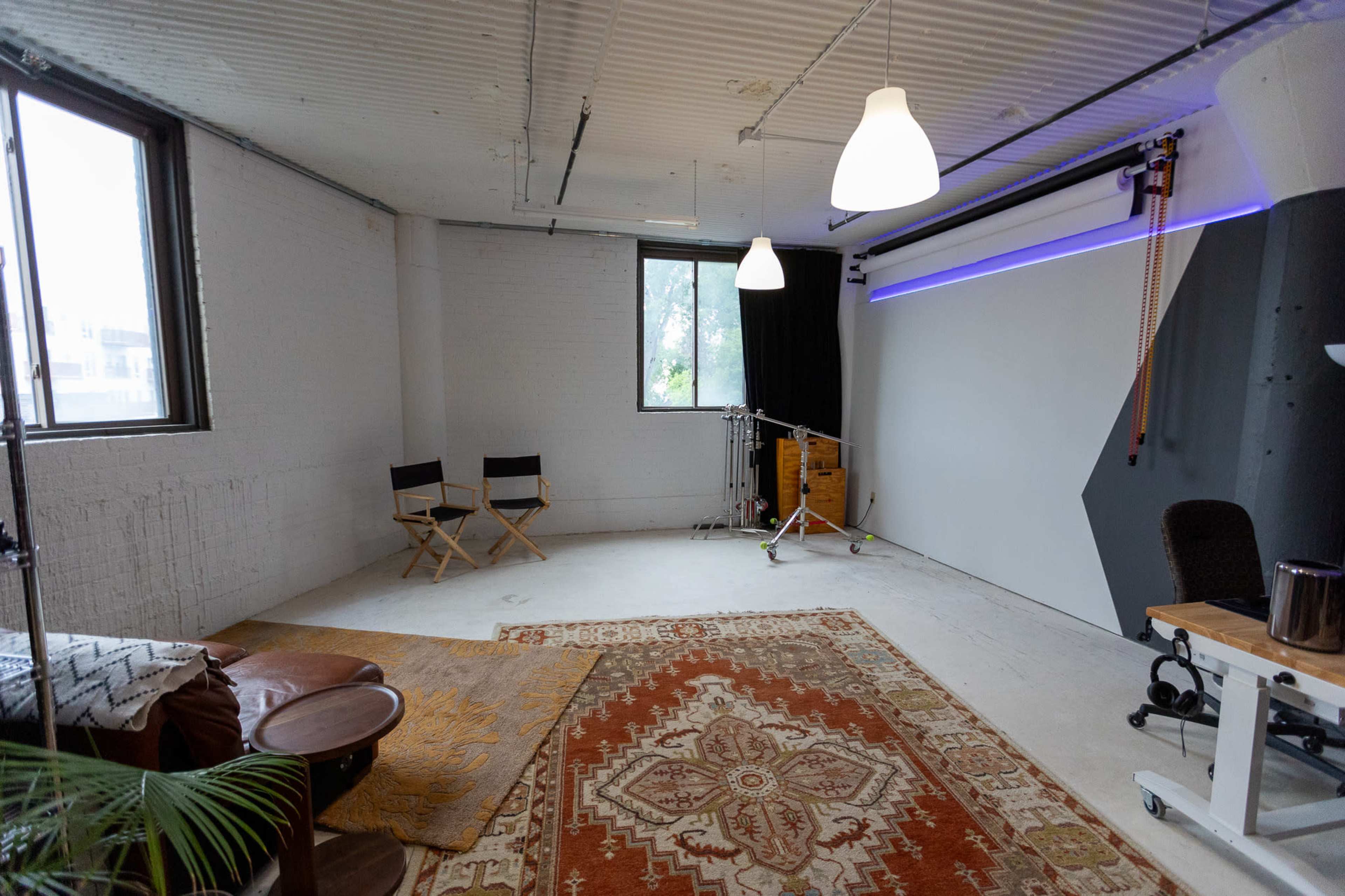 A spacious, minimally furnished studio with two director's chairs, a large area rug, and a backdrop setup against a white wall.