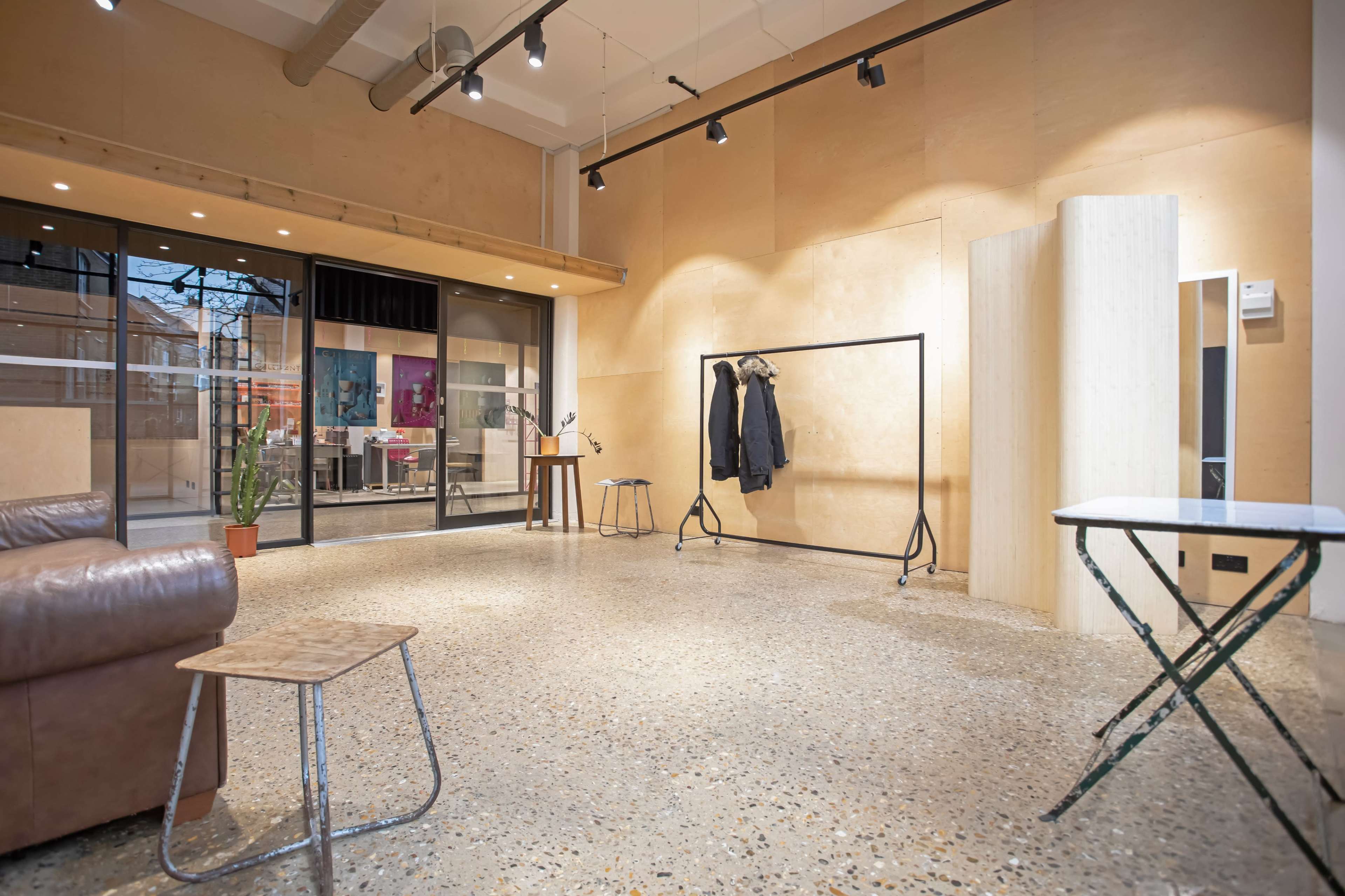 A spacious interior room with wooden walls, polished concrete flooring, a coat rack, a small table, and a pair of mirrors.