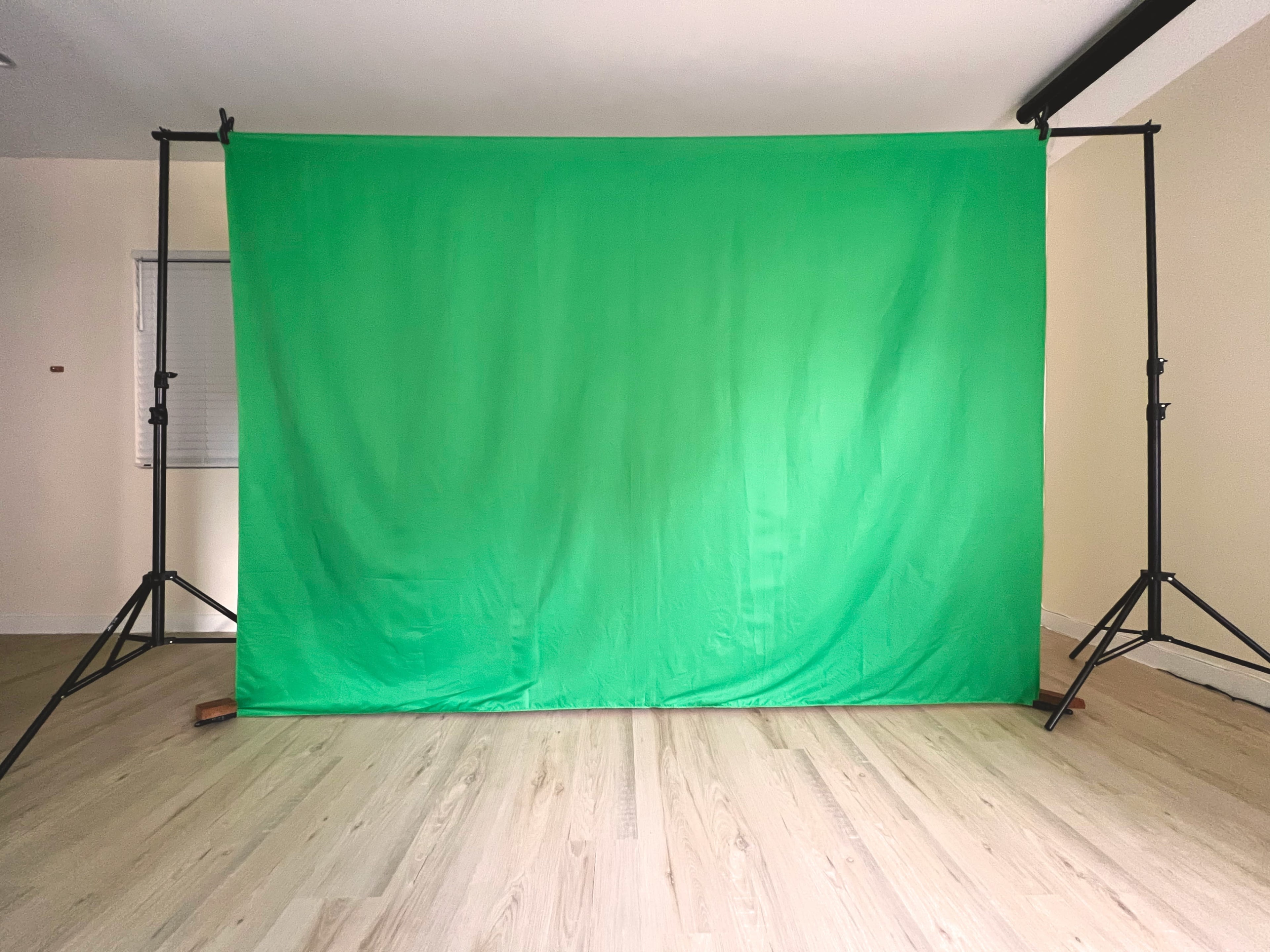 A green backdrop is set up on stands in a minimalist room with light wooden flooring.