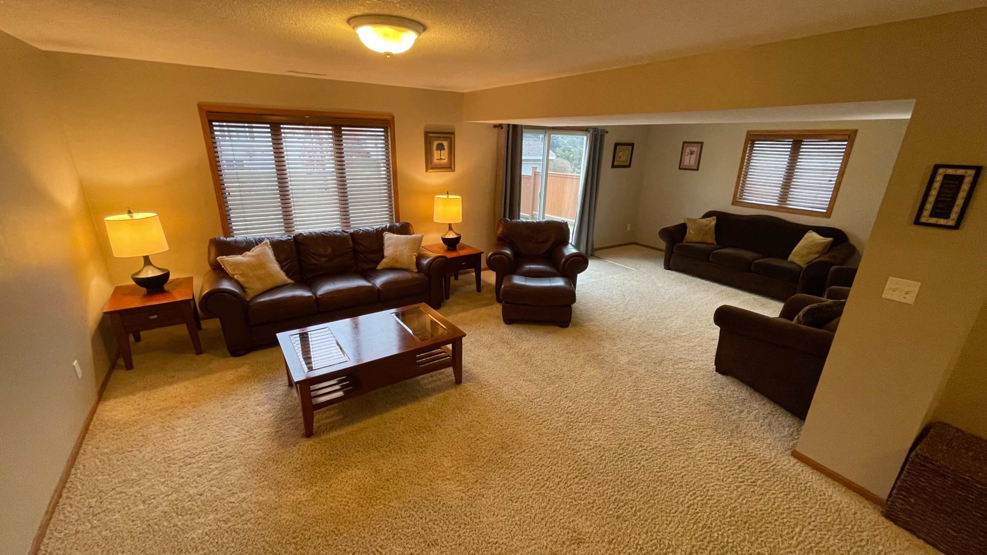 A living room with a seating area that includes a brown leather sofa, an armchair, two lamps on side tables, and a view of a sliding glass door leading to an outdoor space.