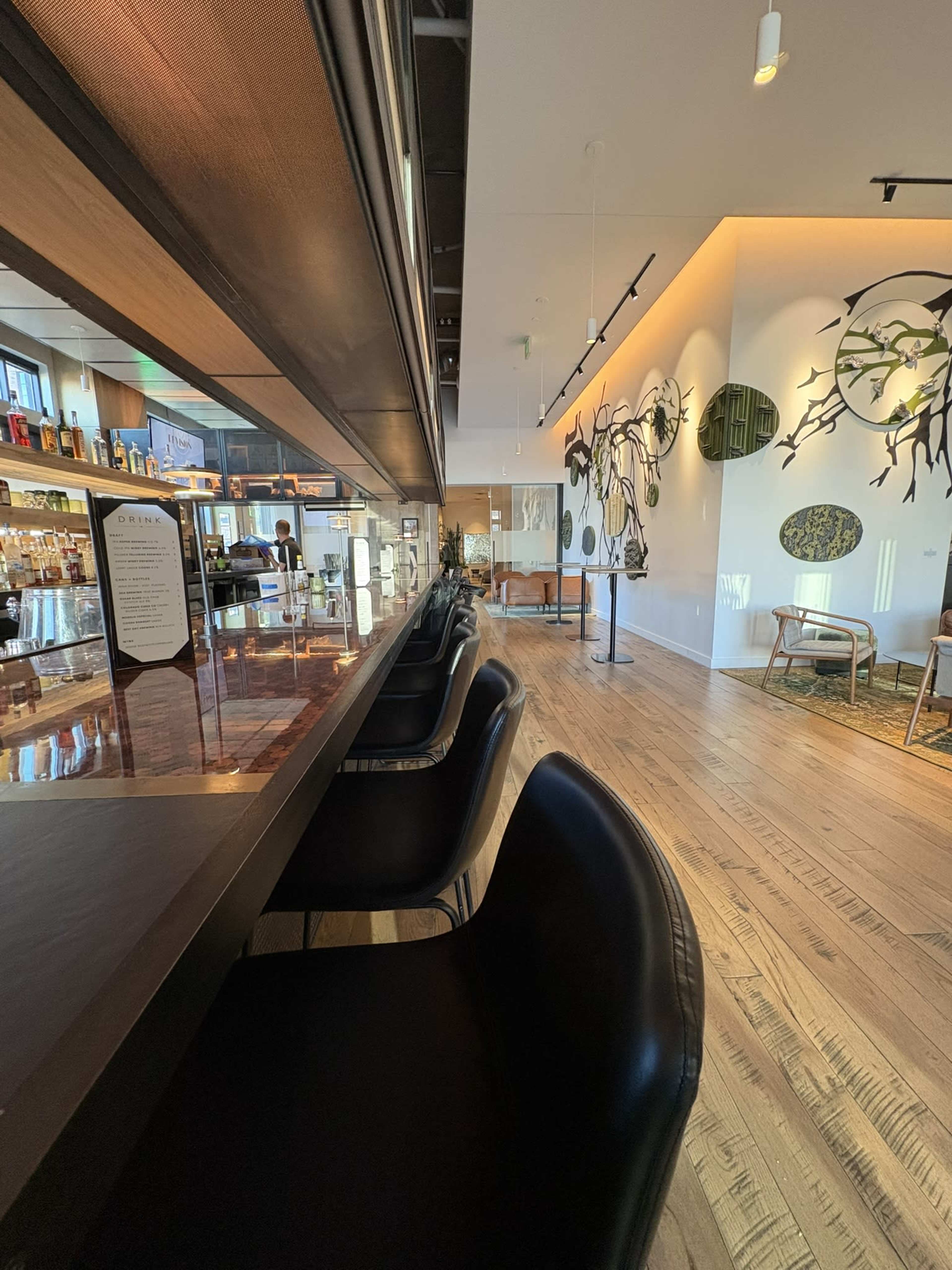 The image shows a modern bar area with high-backed black chairs, a well-stocked bar counter, and artfully designed wall decor.