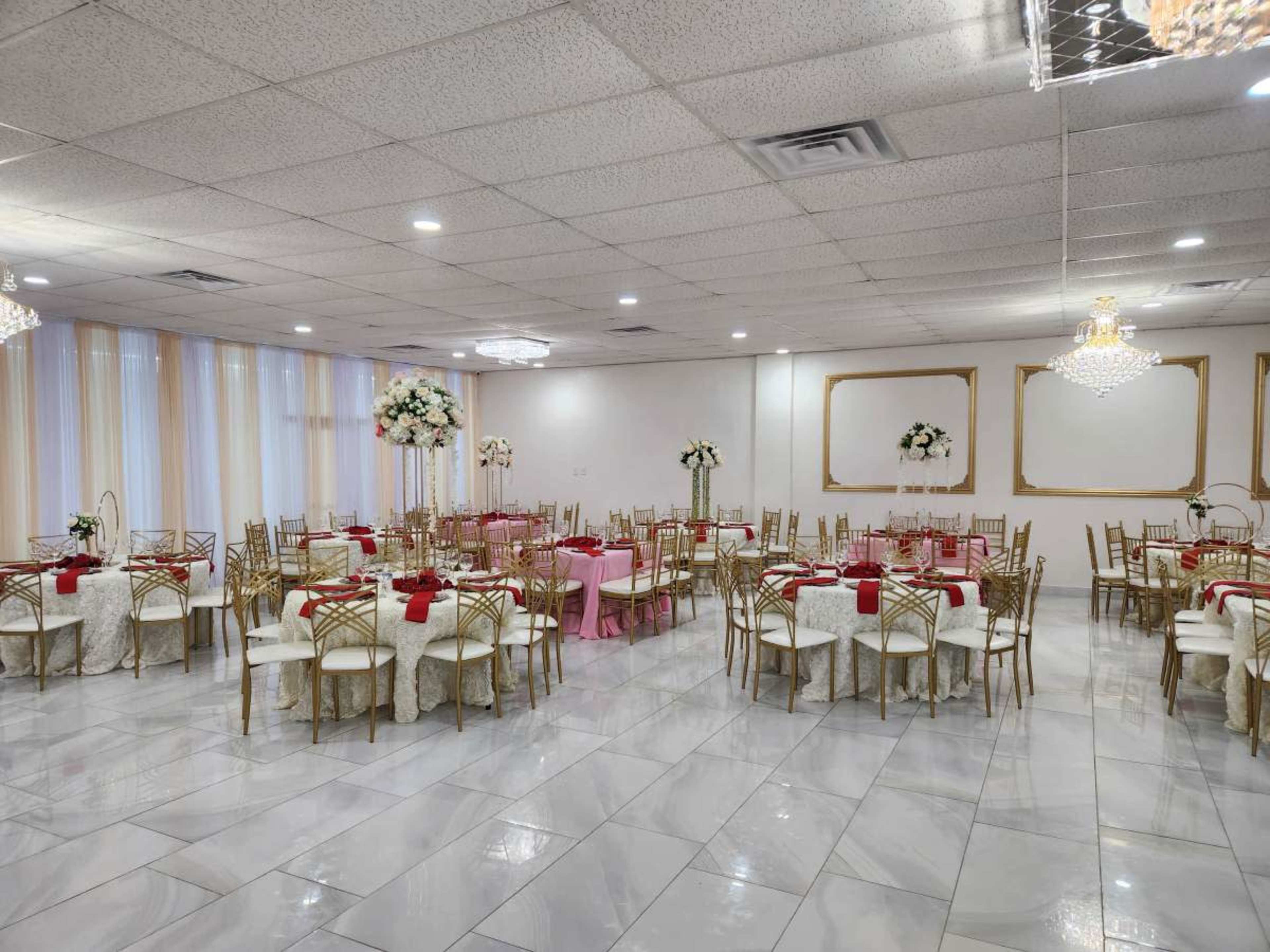 The image shows a large event hall set up for a banquet, featuring round tables adorned with white tablecloths and red napkins, surrounded by gold chairs, and decorated with floral centerpieces.