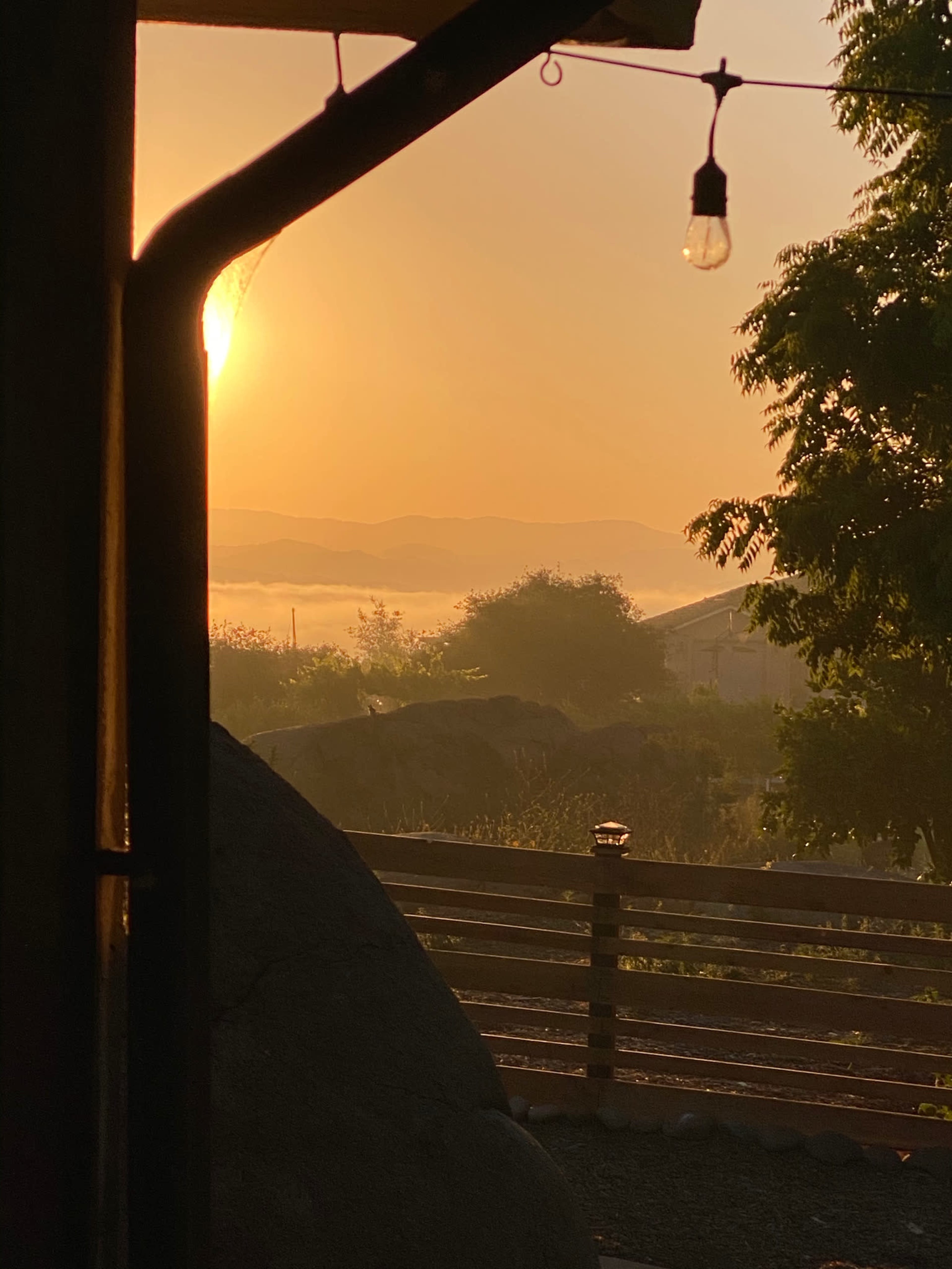 A sunrise over misty mountains, viewed through a structure with a light bulb hanging in the foreground.