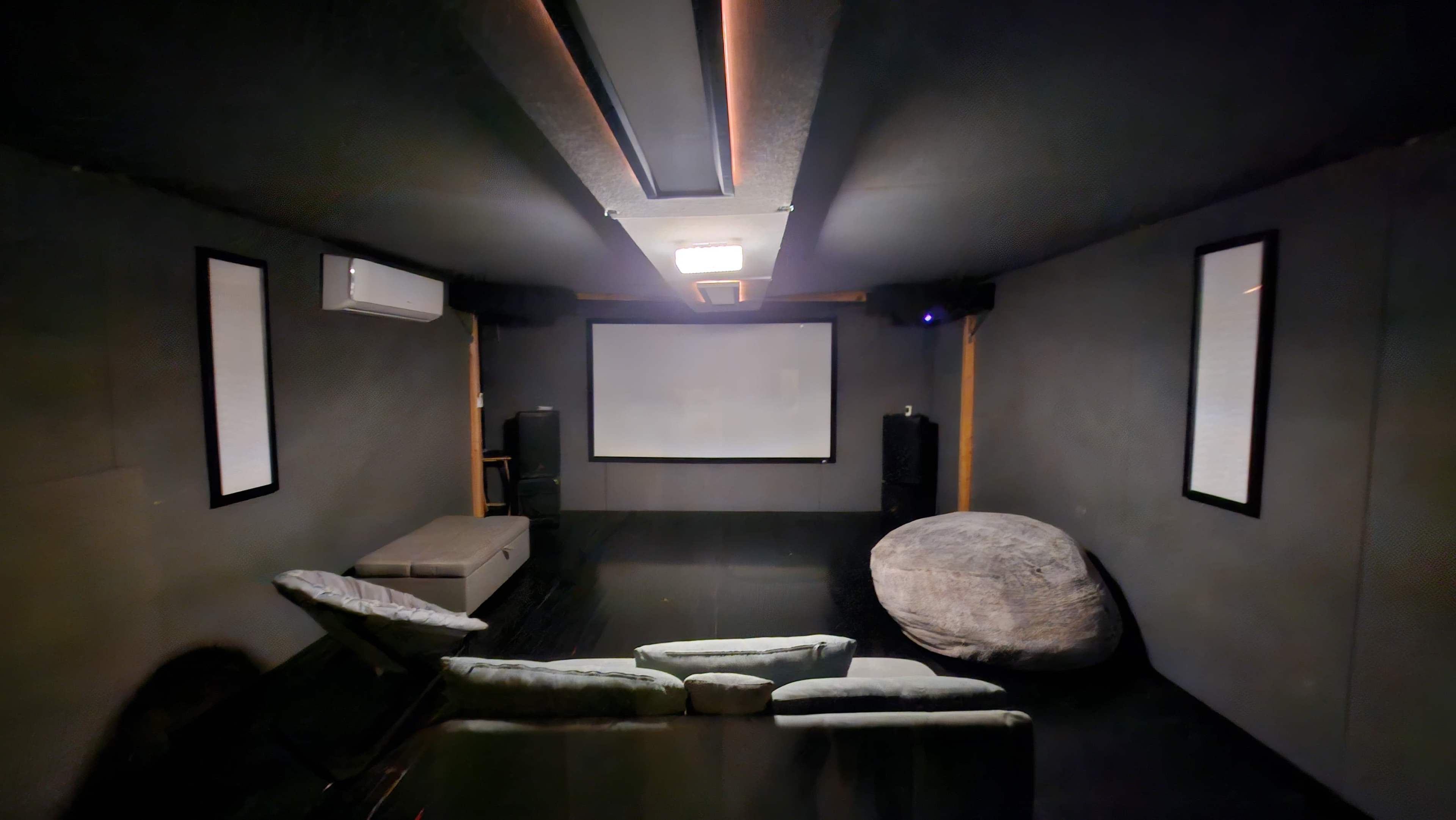 A dark, enclosed home theater room with a large screen at the front, seating arrangements, and sound equipment.