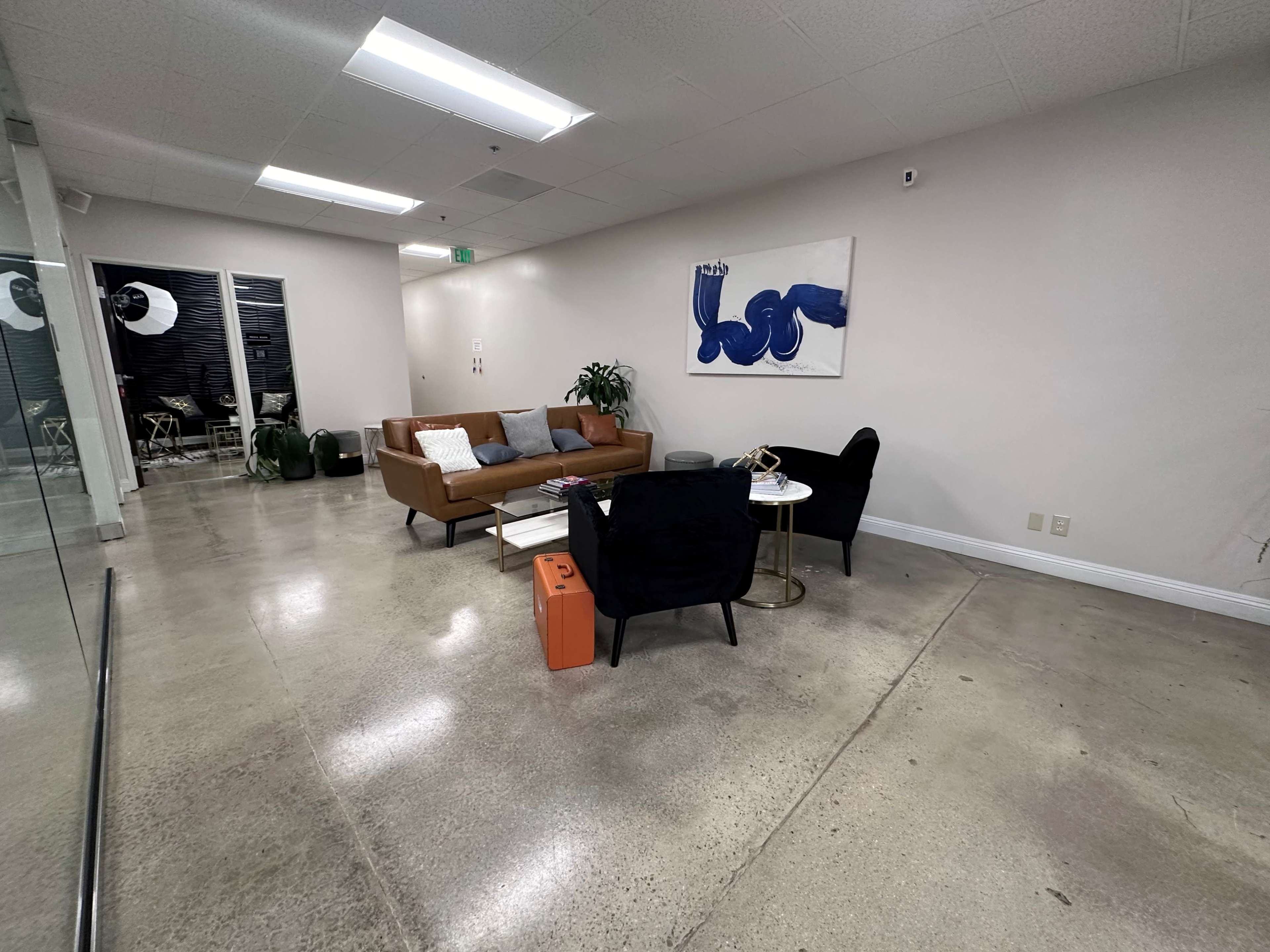 A modern lounge area with a brown sofa, two black chairs, a coffee table, and a piece of artwork on the wall, all set on a polished concrete floor.